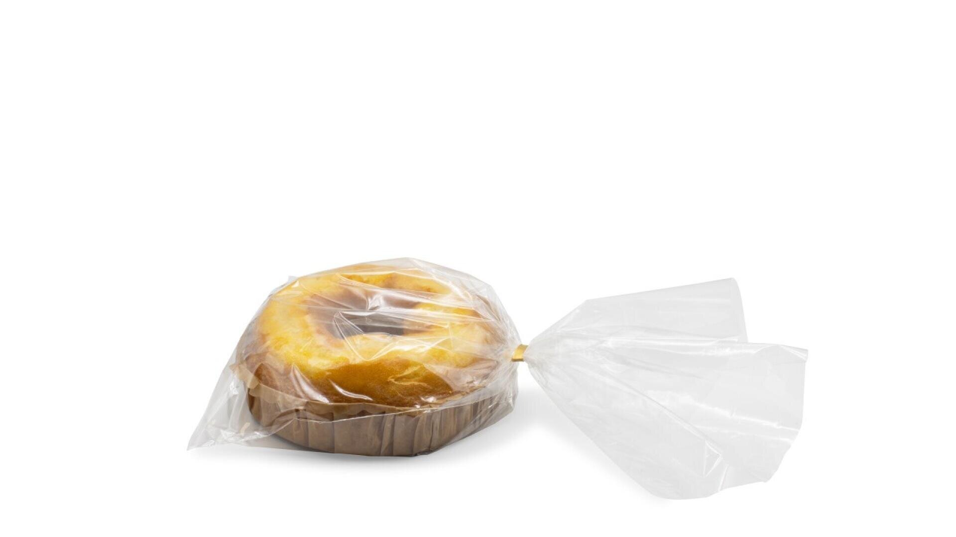 A round loaf of bread in a brown paper tray, wrapped in a partially opened clear plastic bag, set against a plain white background.