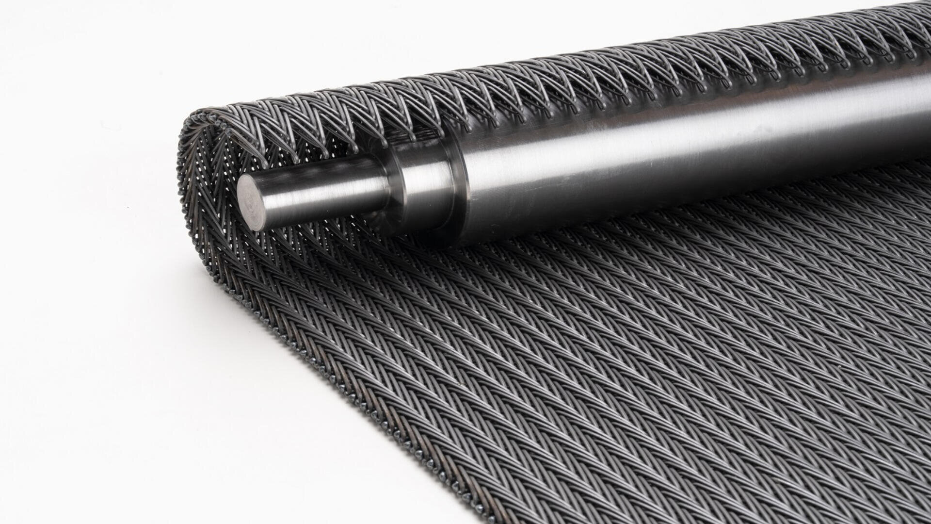 A close-up of a rolled metal conveyor belt with an intricate, interwoven pattern, attached to a cylindrical metal rod, placed on a white background.