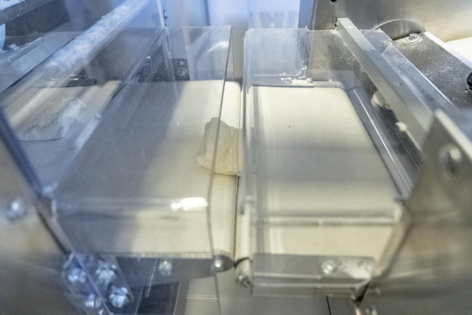 Close-up of a piece of dough being processed through a commercial dough sheeter machine with transparent plastic covers.