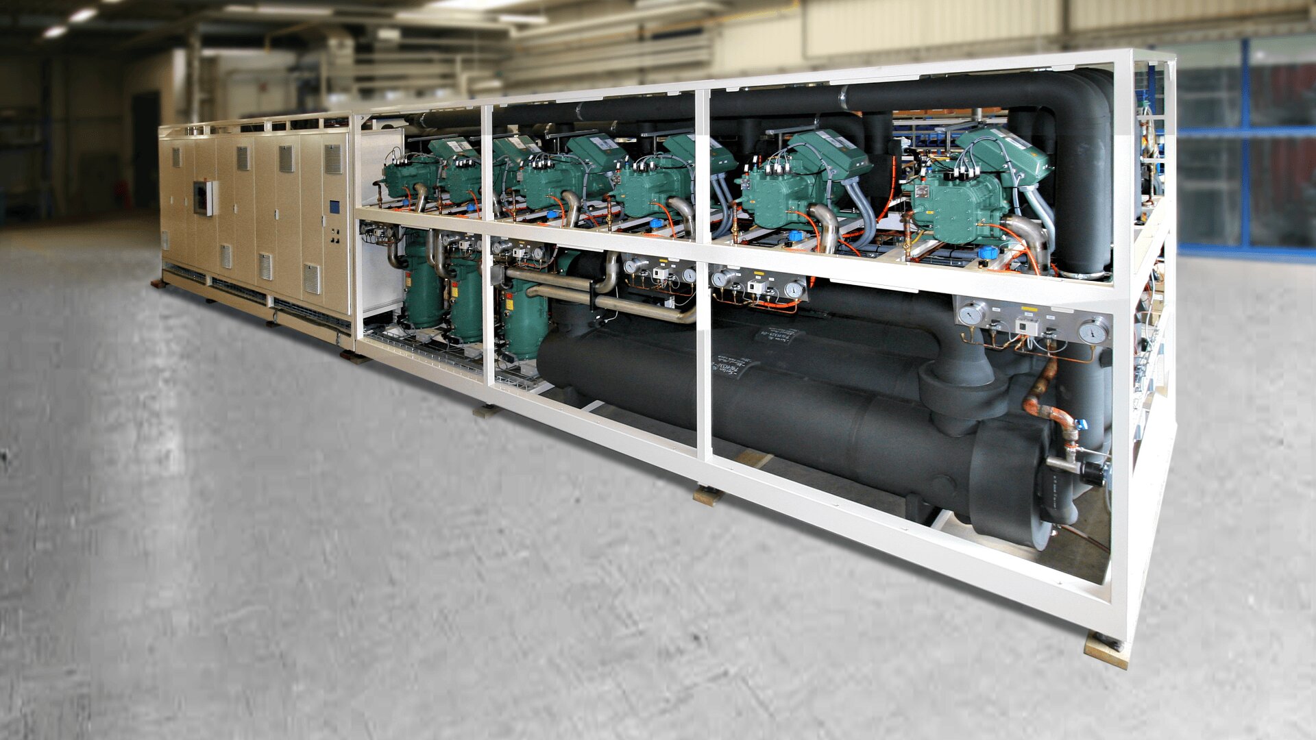 Large industrial refrigeration unit with multiple green compressors, black cylindrical tanks, and copper piping mounted on a white metal frame inside a spacious warehouse.