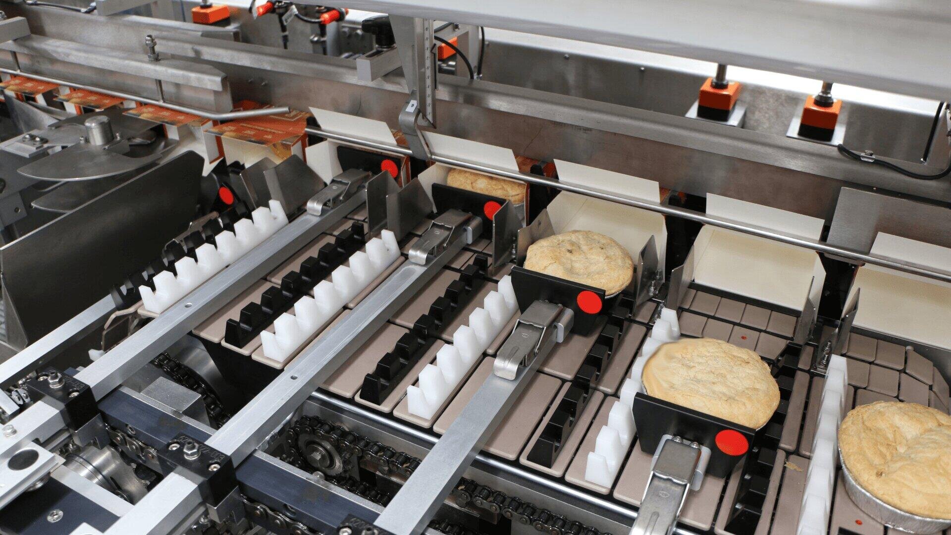 Several loaves of bread move along an automated conveyor system in a bakery production line, surrounded by metal machinery and sorting mechanisms.