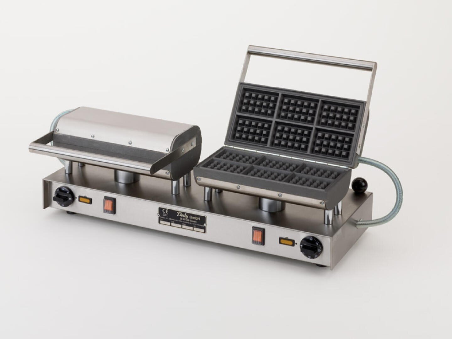 Ein kommerzielles Waffeleisen aus Edelstahl mit zwei Waffelplatten, von denen eine offen ist und das Gittermuster zeigt und die andere geschlossen ist, mit Bedienknöpfen, Schaltern und Kontrollleuchten auf der Vorderseite.