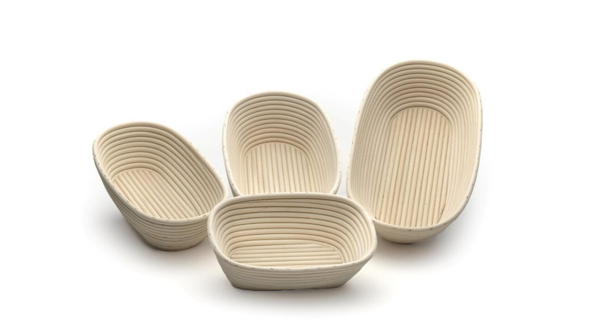Four empty oval-shaped banneton bread proofing baskets of varying sizes are arranged on a white background. The baskets have a ribbed pattern and are made of light-colored material.