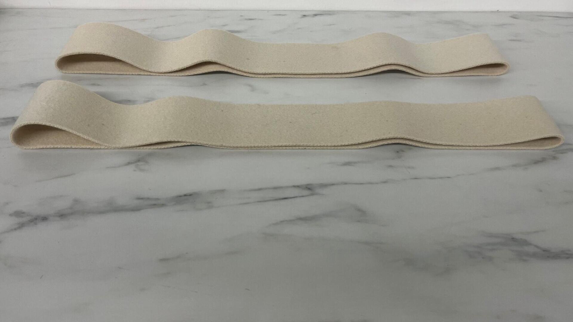 Two beige, fabric strips with wavy, folded shapes lie parallel on a white marble surface.
