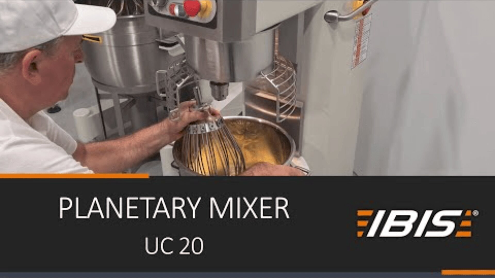 A person places a whisk attachment into a large industrial planetary mixer filled with batter. The machine is labeled “IBIS,” and text on the image reads: “PLANETARY MIXER UC 20.”.