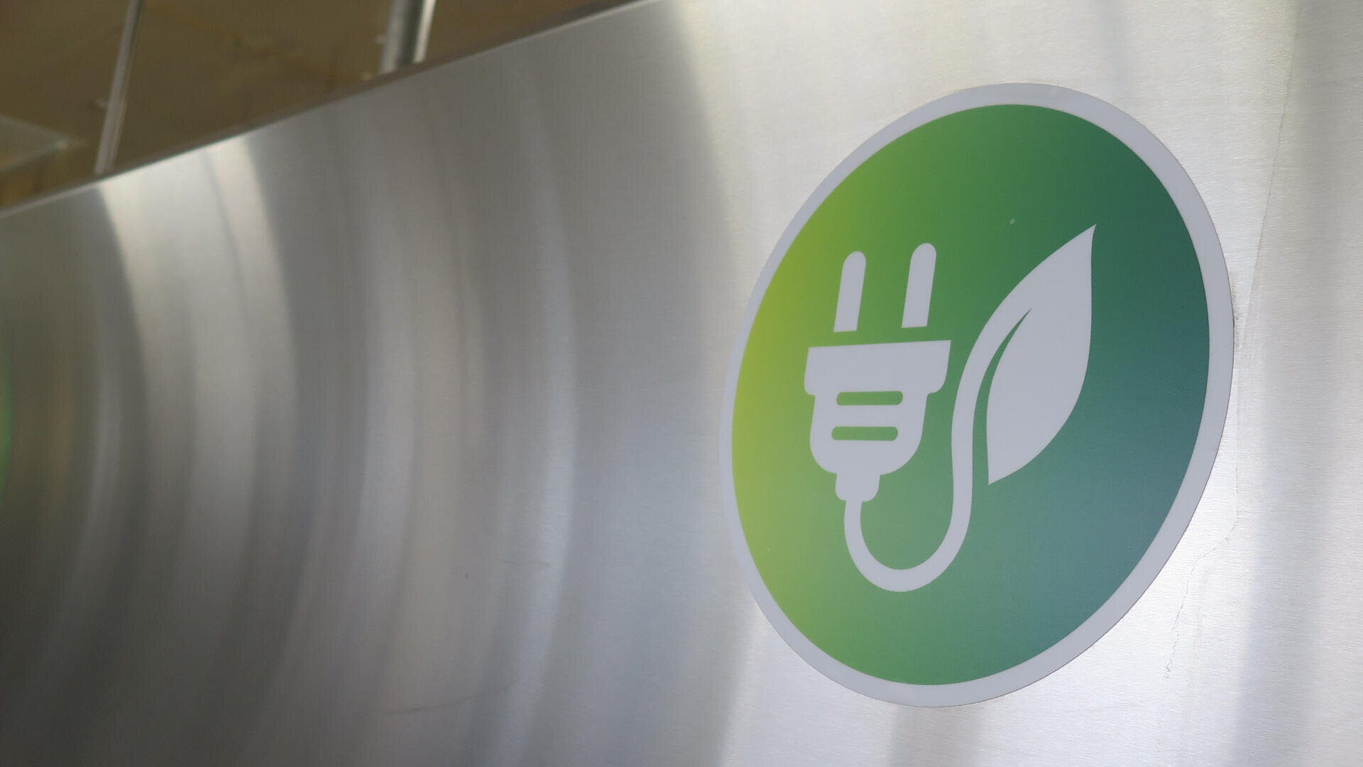 A green circular sign with a white electrical plug and a leaf, symbolizing eco-friendly or clean energy, is displayed on a metallic surface.