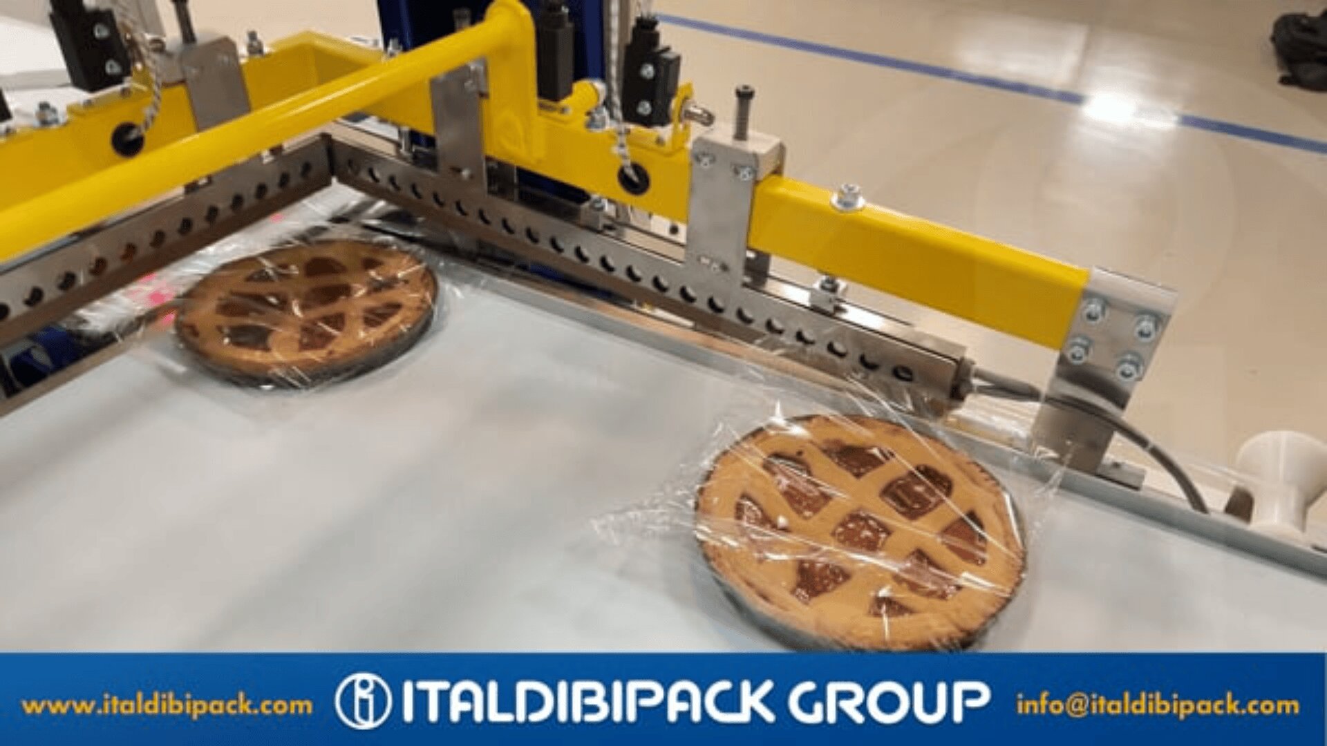 Two lattice-topped pies are being wrapped in clear plastic by an automated packaging machine. The machine is yellow and silver. The bottom of the image displays the ITALDIBIPACK GROUP logo and website information.