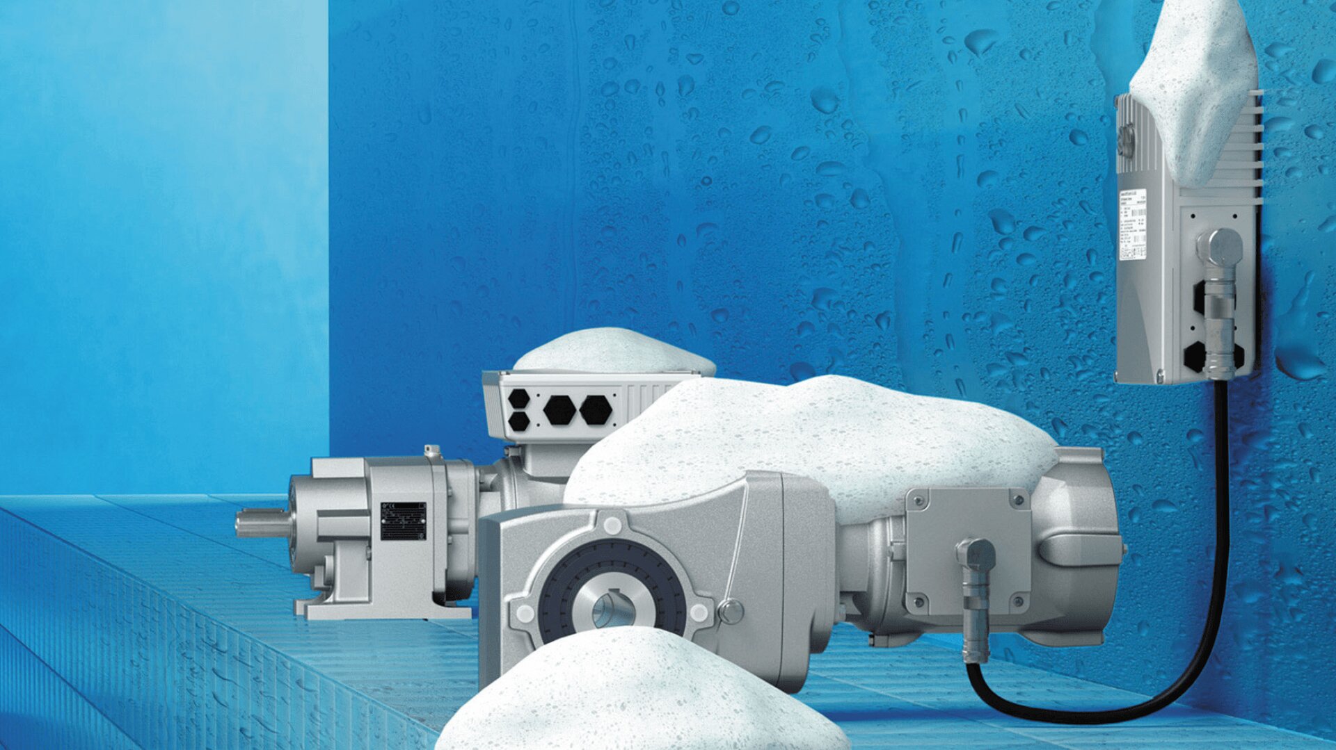 Industriemaschinen, einschließlich eines Getriebemotors und einer Steuereinheit, bedeckt mit weißem Schaum und Wassertröpfchen vor einem blauen Hintergrund, was auf eine Reinigung oder Abwaschung in einer feuchten Umgebung hindeutet.