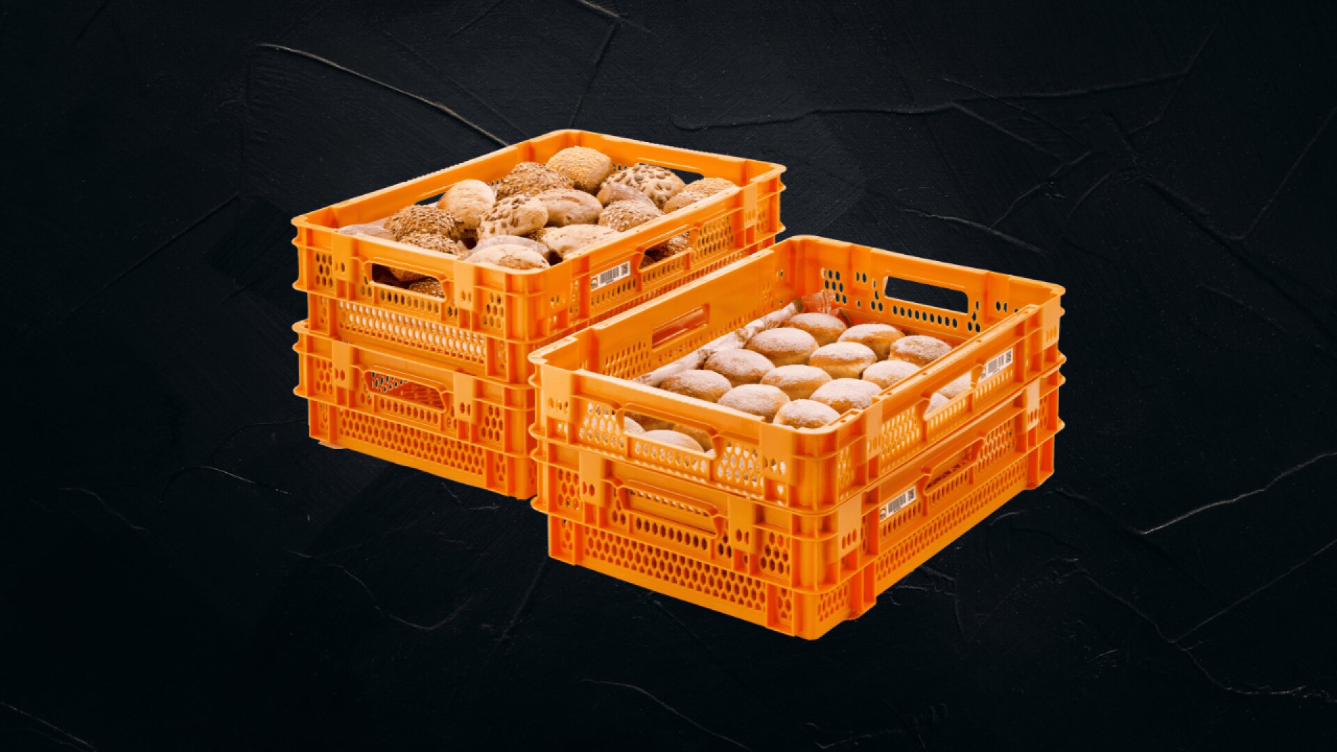 Zwei orangefarbene Plastikkisten, gefüllt mit verschiedenen Brötchen, nebeneinander vor einem dunkel strukturierten Hintergrund.