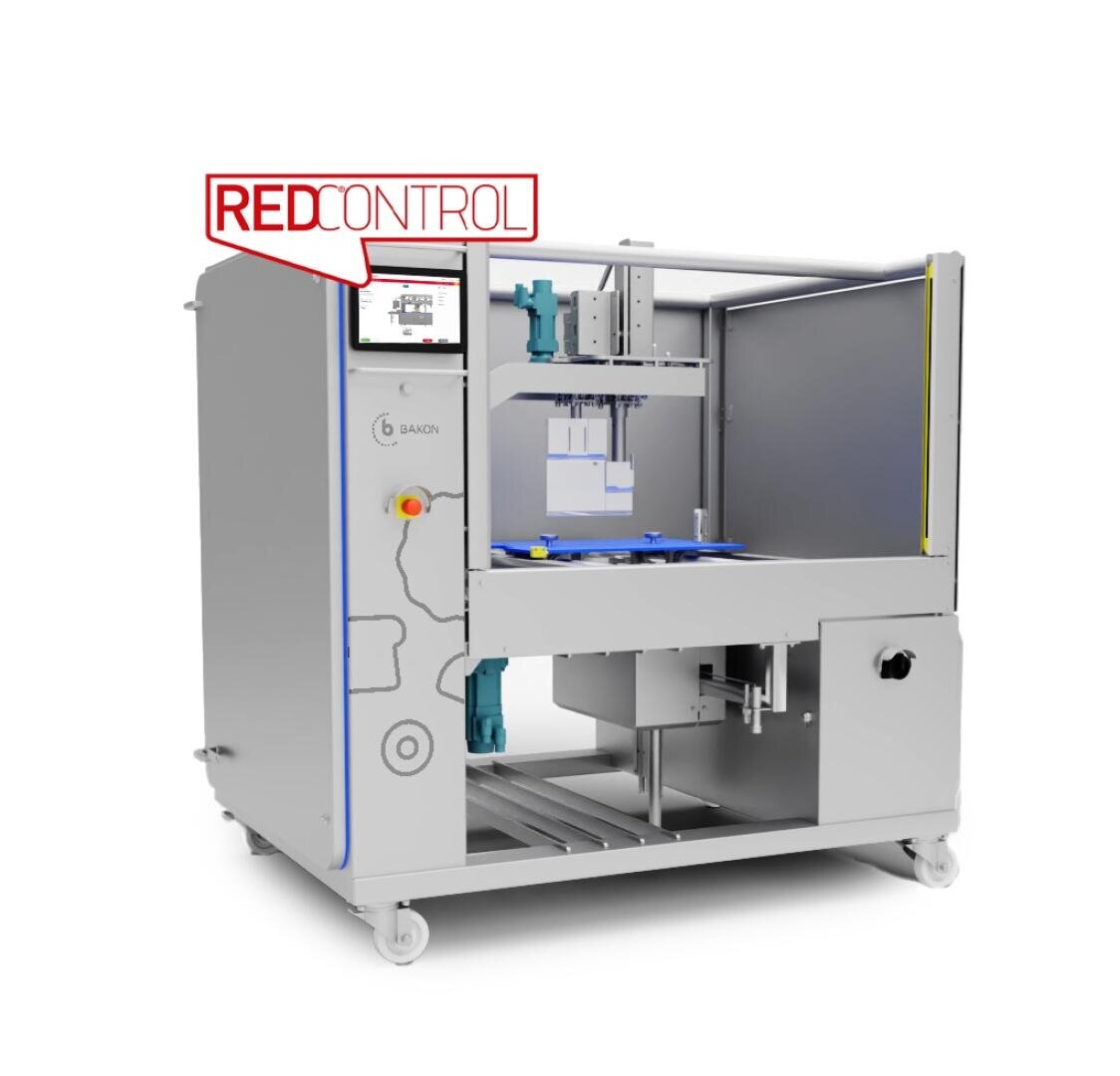A large industrial machine with a digital display labeled REDCONTROL. The machine has metallic panels, wheels, and an open compartment revealing internal mechanisms and blue trays inside.