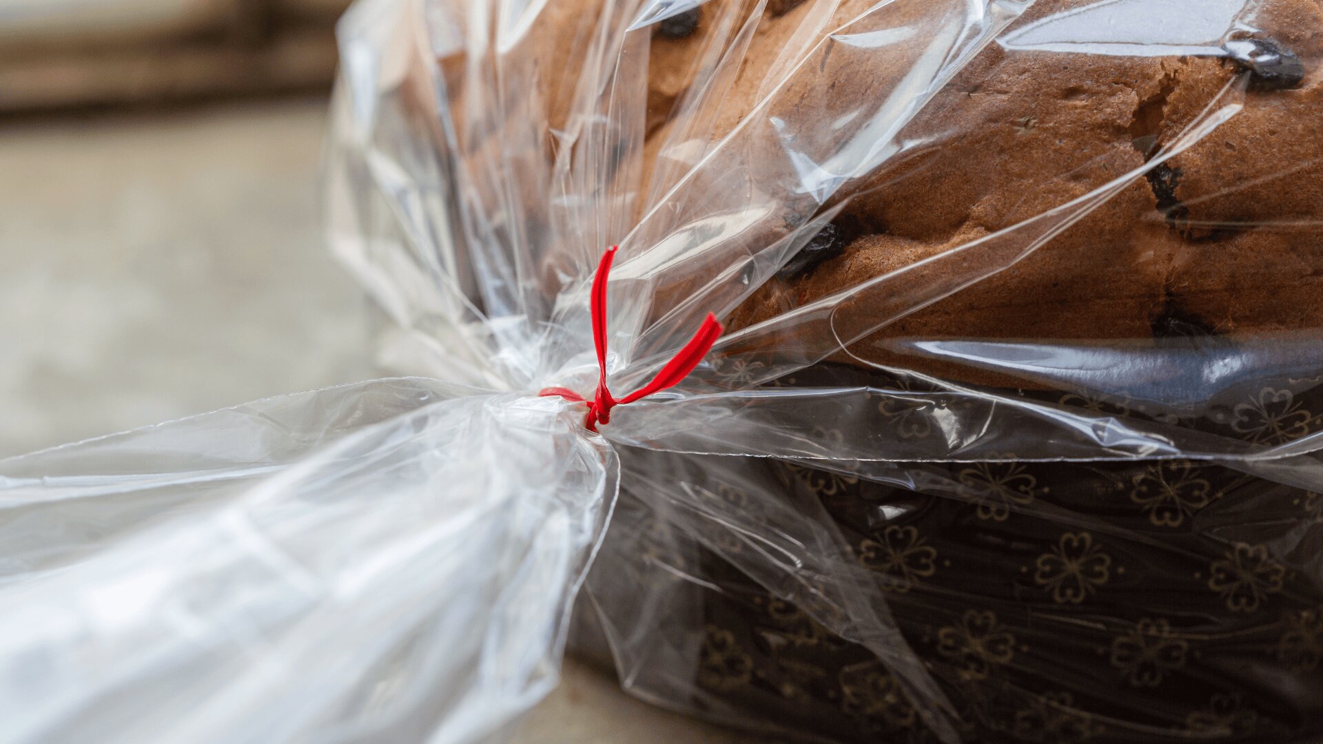 A loaf of bread in a patterned brown tray, wrapped in clear plastic and secured with a red twist tie.