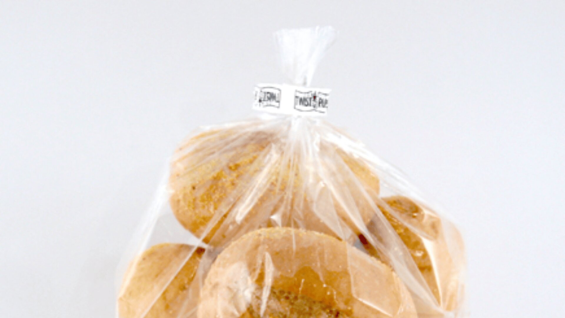 A clear plastic bag filled with round sandwich buns or rolls is tied at the top with a twist tie against a plain white background.