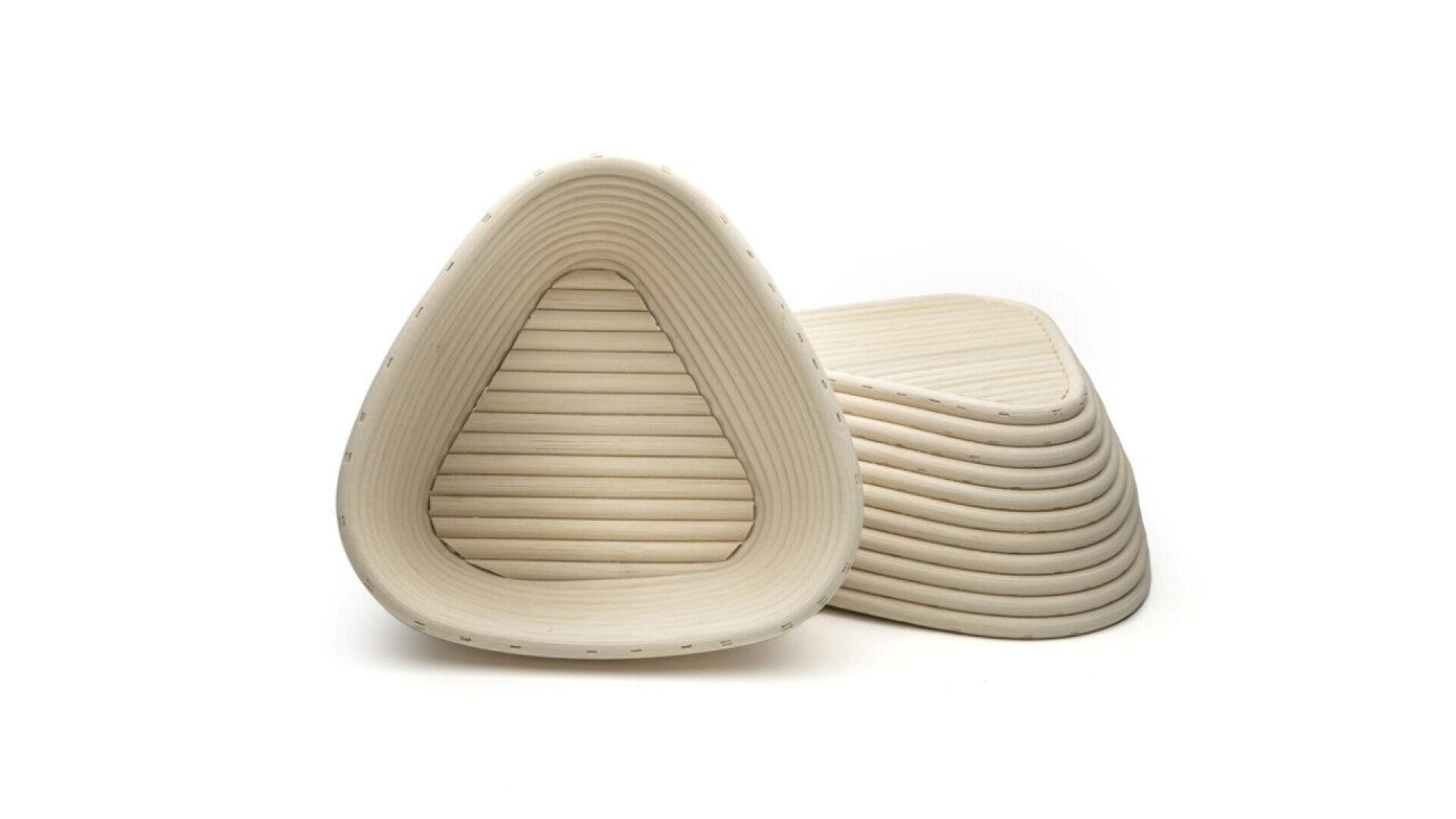 A stack of triangular, ribbed, light-colored bread proofing baskets made of woven material, with one basket standing upright in front of the stack, all set against a white background.