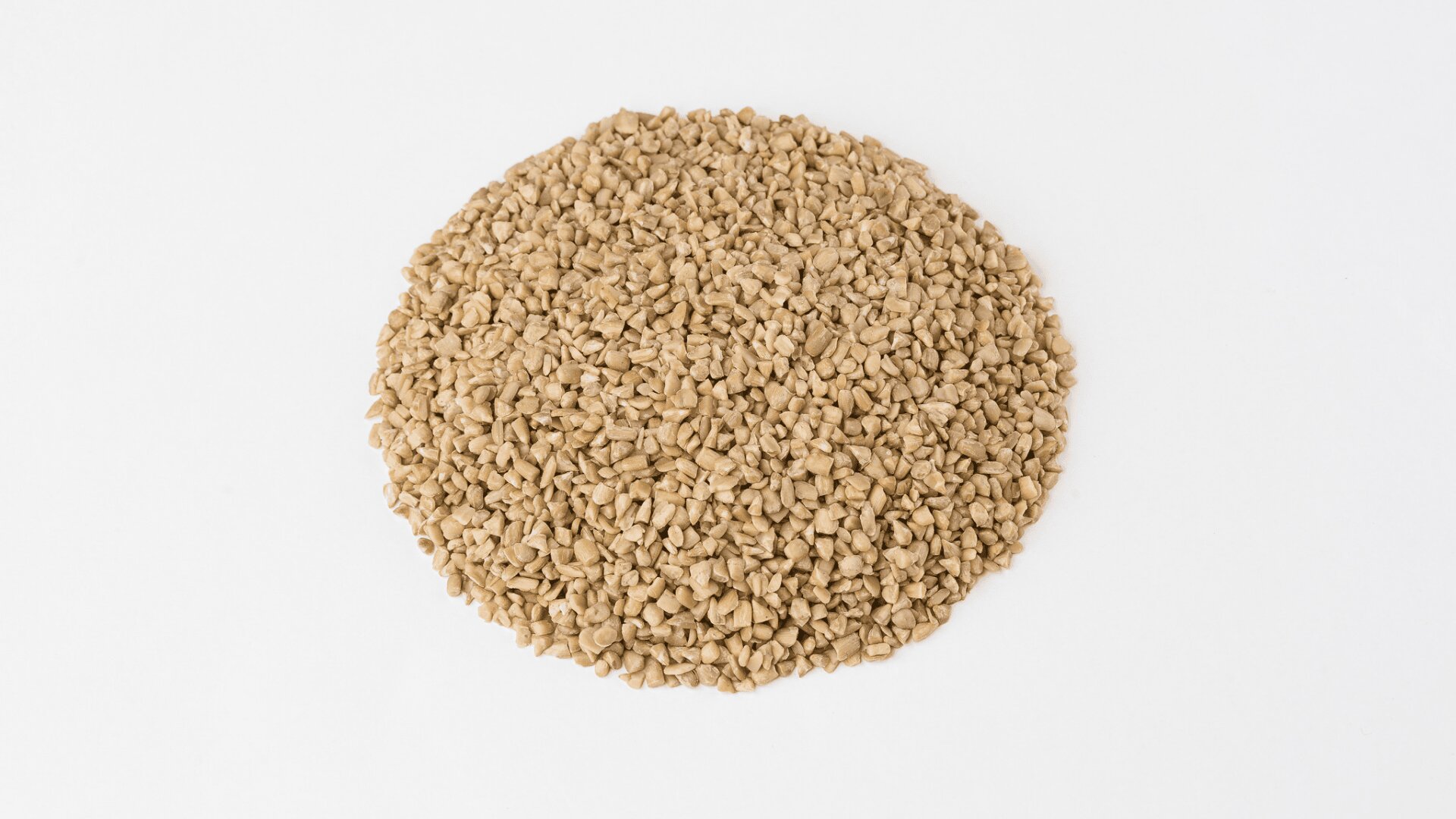 A round, flat pile of light brown, uncooked buckwheat groats is spread out on a white background.