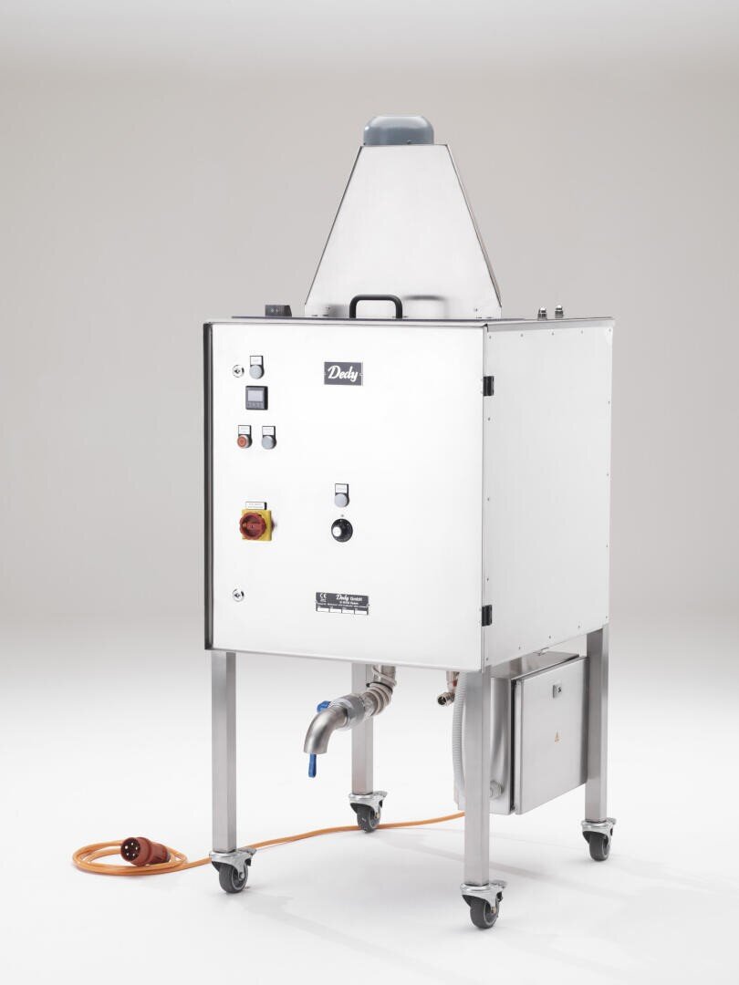 Ein weißes, industrielles Gerät auf Rädern mit Bedienknöpfen, einem belüfteten Oberteil, angeschlossenen Schläuchen und einem orangefarbenen Stromkabel auf dem Boden; die Marke Dandy ist auf der Vorderseite aufgedruckt.