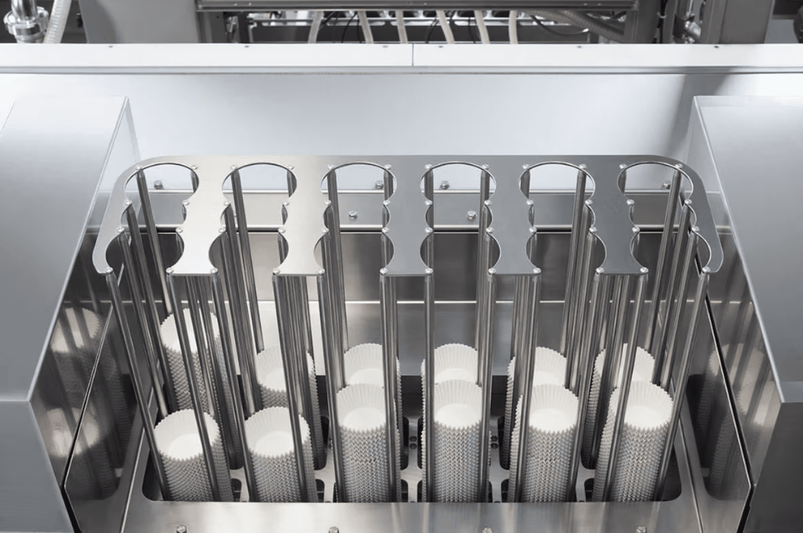 Nahaufnahme einer automatisierten Maschine, die mit Reihen leerer weißer Papierförmchen für Muffins oder Cupcakes gefüllt ist, die ordentlich in Metallhaltern angeordnet und für die Produktion in einer Lebensmittelverarbeitungsanlage bereit sind.