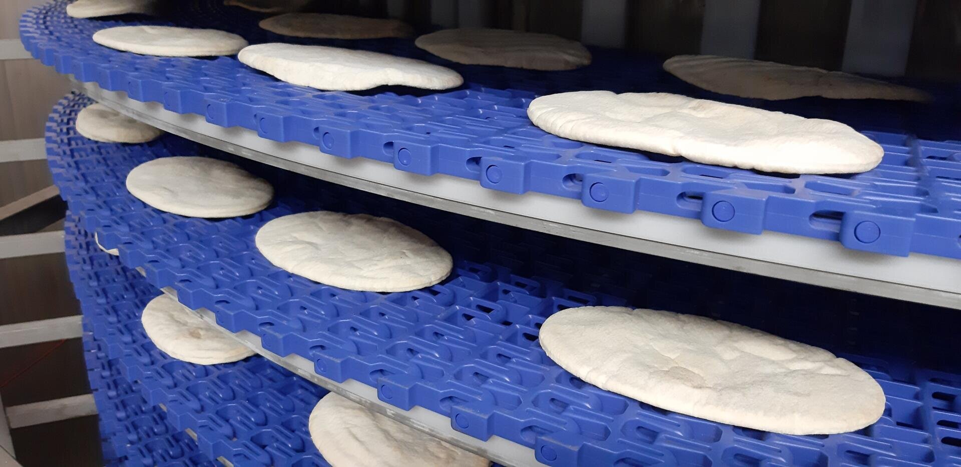 Mehrere Fladenbrotstücke laufen über ein blaues Spiralförderband in einer Lebensmittelverarbeitungsanlage.