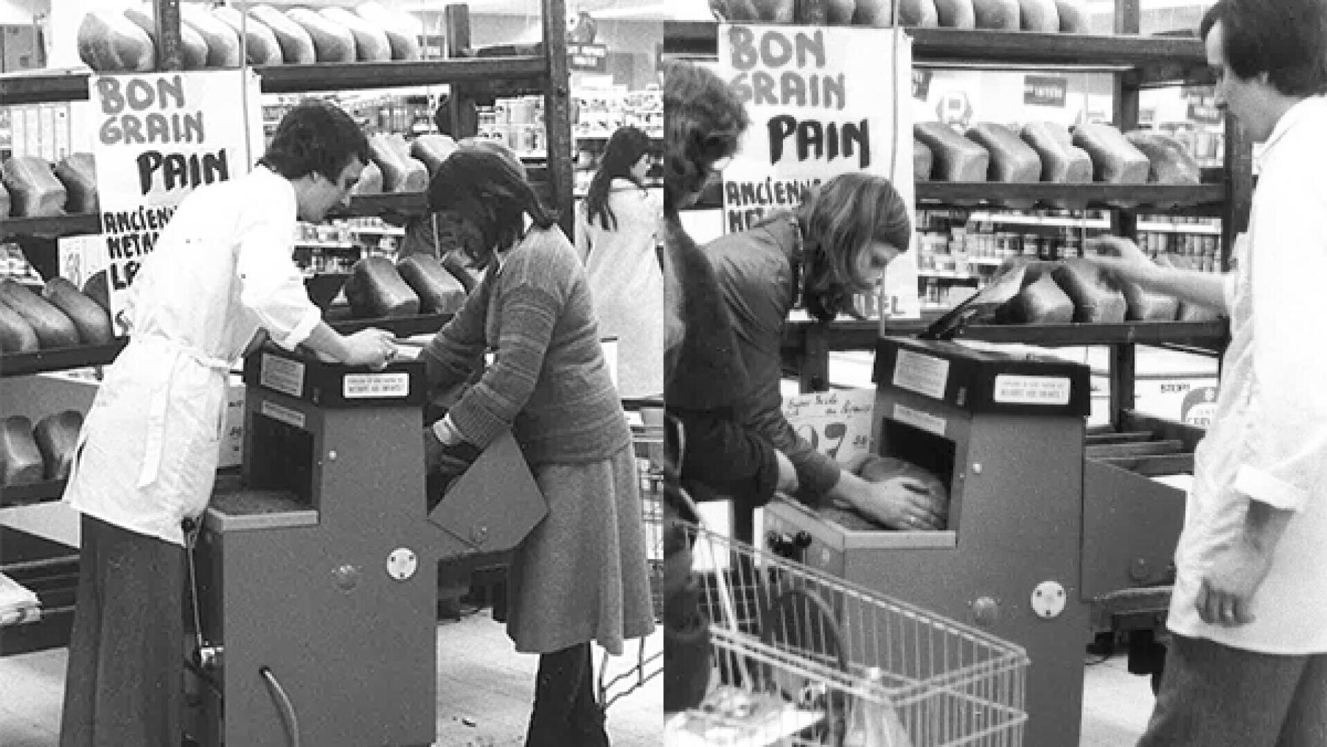 Black and white photo of people using a bread slicing machine at a bakery section in a store. Loaves are displayed on shelves above, with a Bon Grain Pain sign in the background.