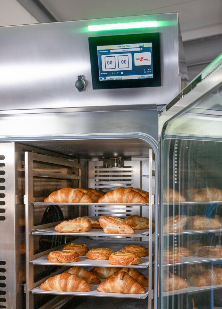 Frisch gebackene Croissants auf mehreren Blechen in einem handelsüblichen Backofen aus Edelstahl mit einem digitalen Bedienfeld, das die Einstellungen oben anzeigt.