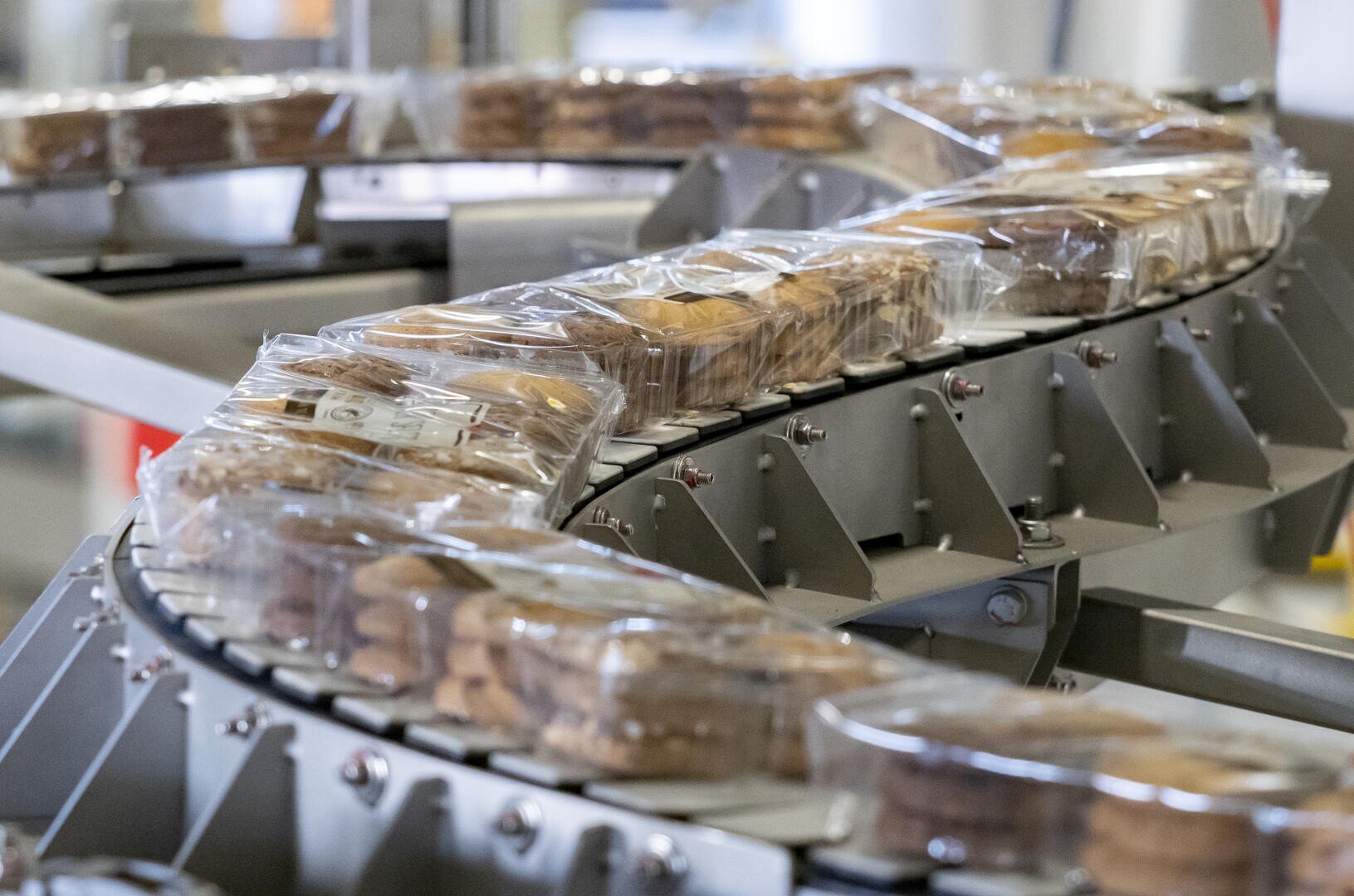 Plastic-wrapped packages of cookies move along a curved conveyor belt inside a food processing or packaging facility.