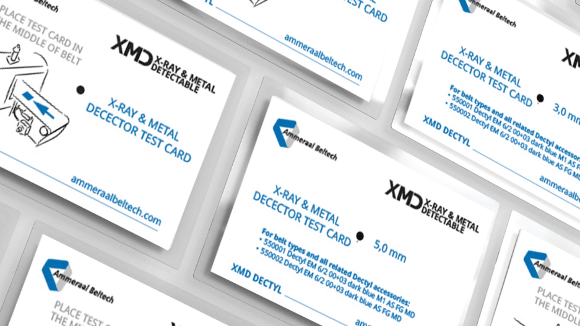 A scattered arrangement of white rectangular cards labeled X-Ray & Metal Detector Test Card with blue and black text and logos from Anmeral Beltech, displayed on a light surface.