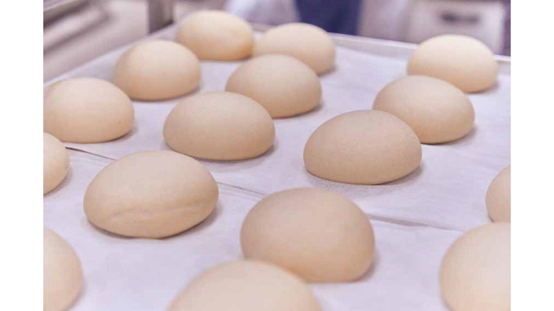 Several smooth, round balls of dough are arranged on a baking tray lined with parchment paper, ready for baking or proofing.