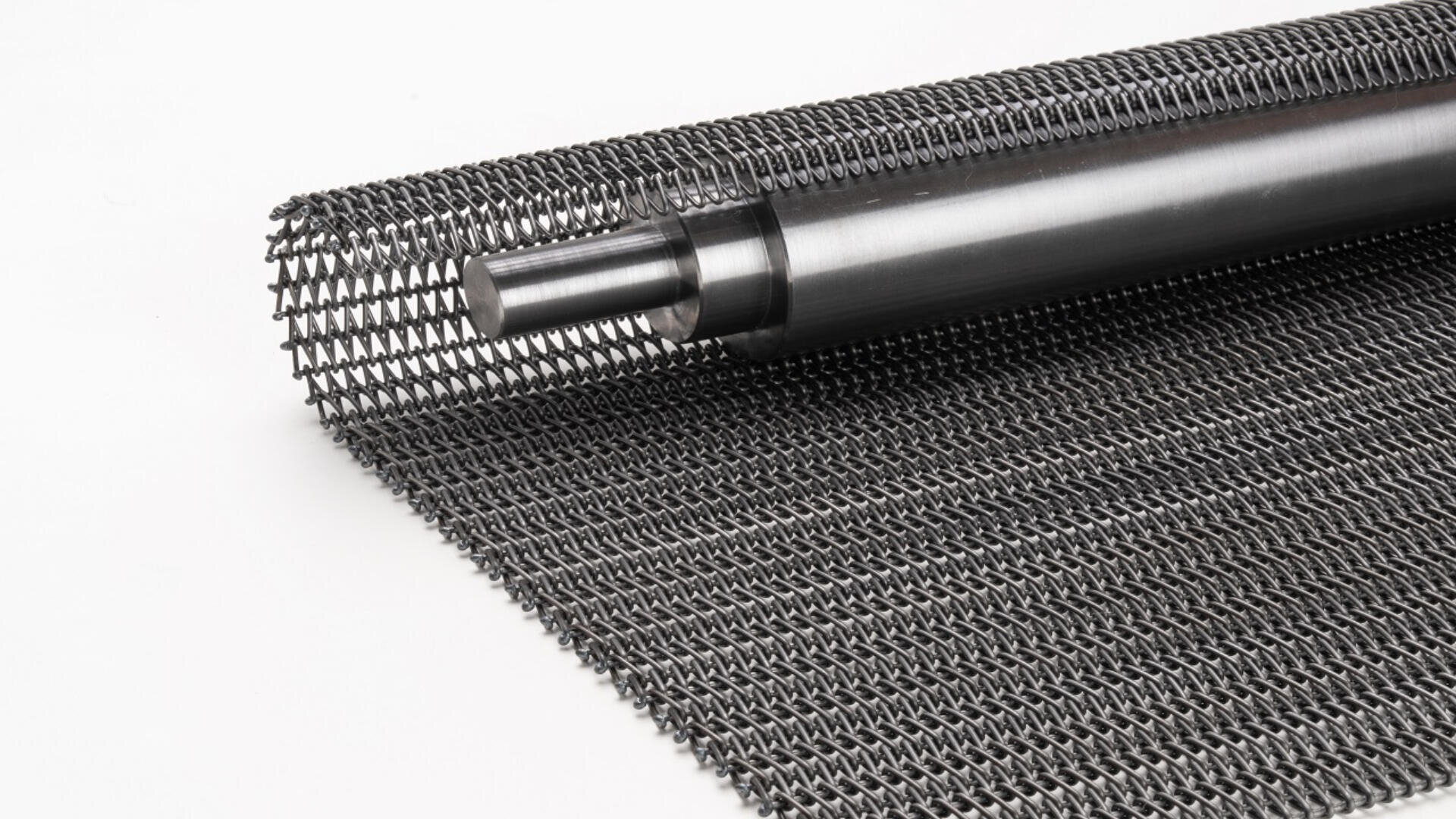 A close-up of a rolled metal wire mesh conveyor belt with a cylindrical metal rod, displayed on a white background.
