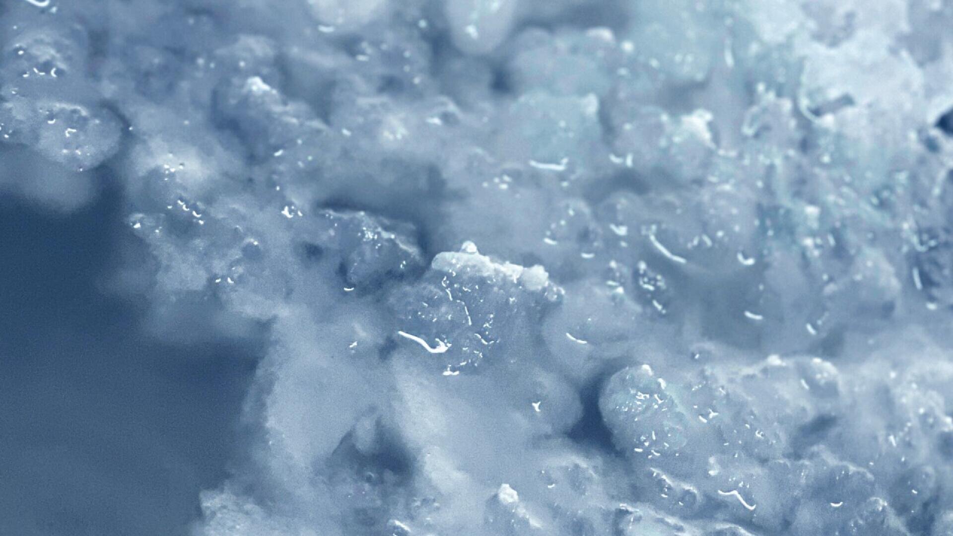 A close-up view of crushed ice, showing glistening, irregularly shaped ice crystals with a frosty, blue-tinted appearance.