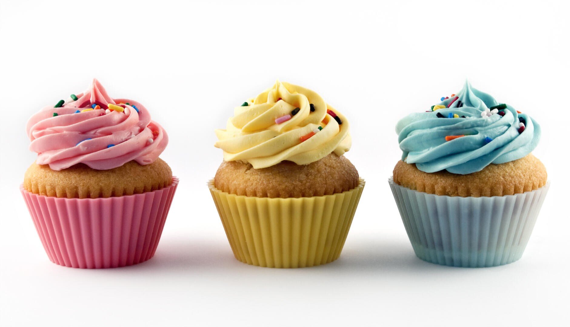 Three cupcakes with colorful frosting—pink, yellow, and blue—each topped with rainbow sprinkles and placed in matching paper wrappers against a white background.