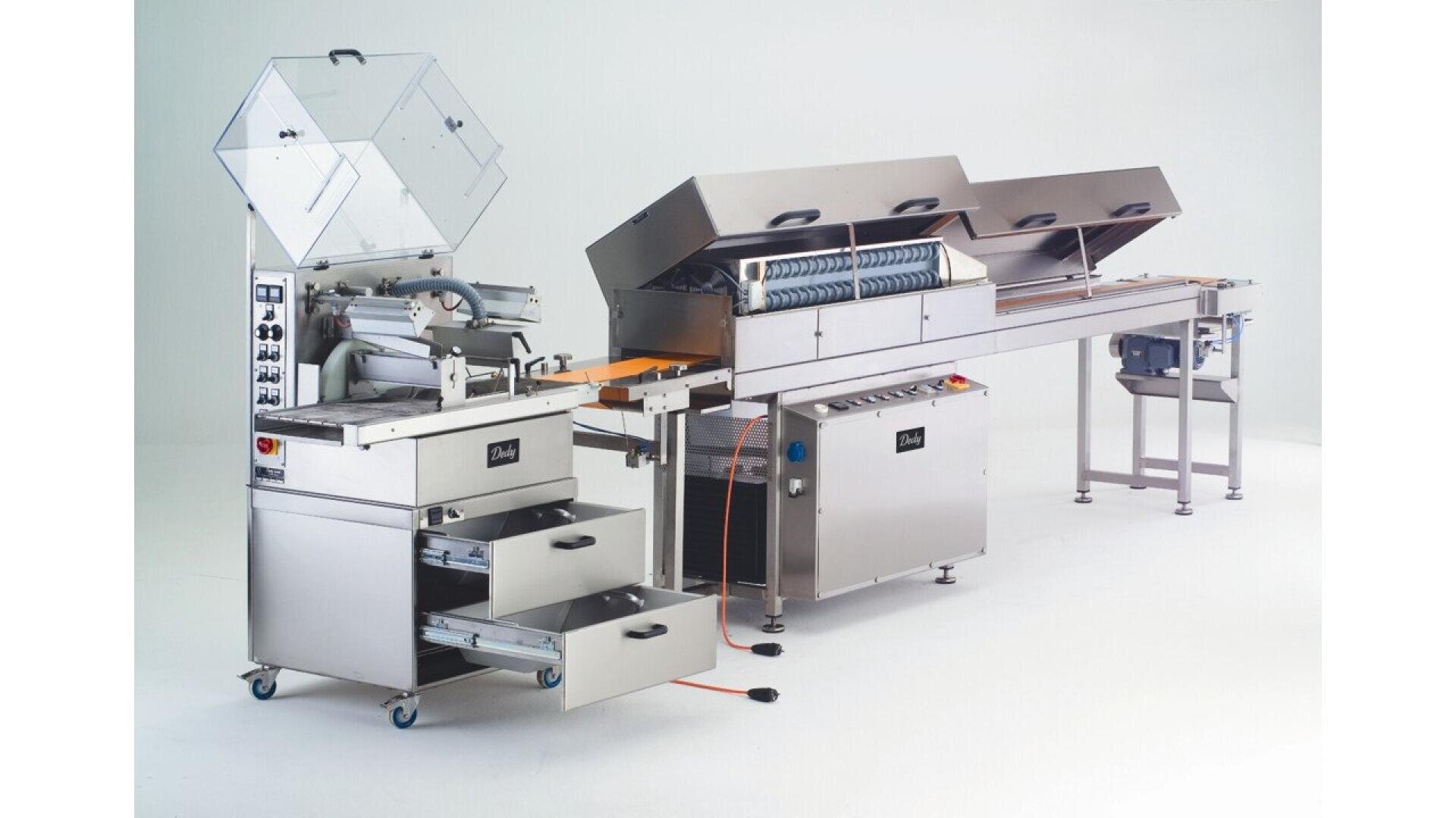 A stainless steel commercial food processing machine with control panels, conveyor belts, and multiple compartments, used for automated food production in an industrial setting.