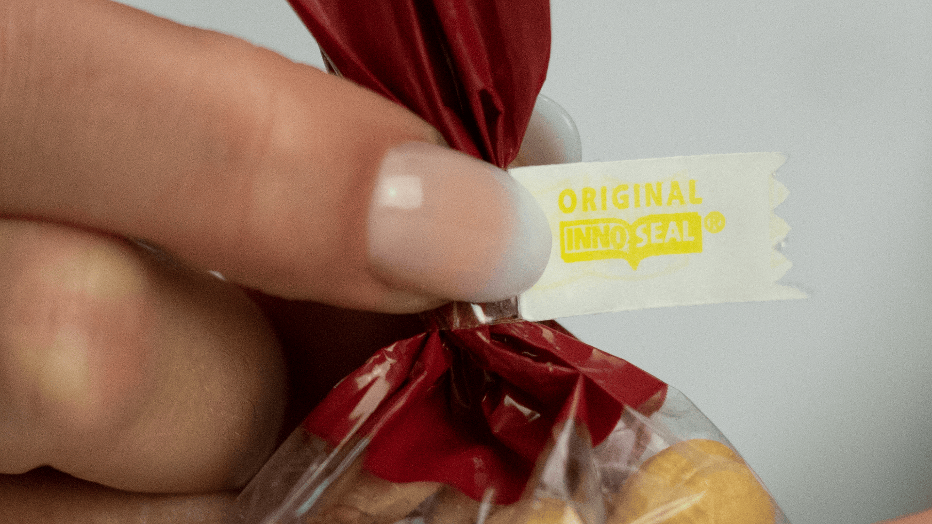 A hand with manicured nails holds a red-twist plastic bag sealed with a white tag that reads ORIGINAL INNO SEAL in yellow text.