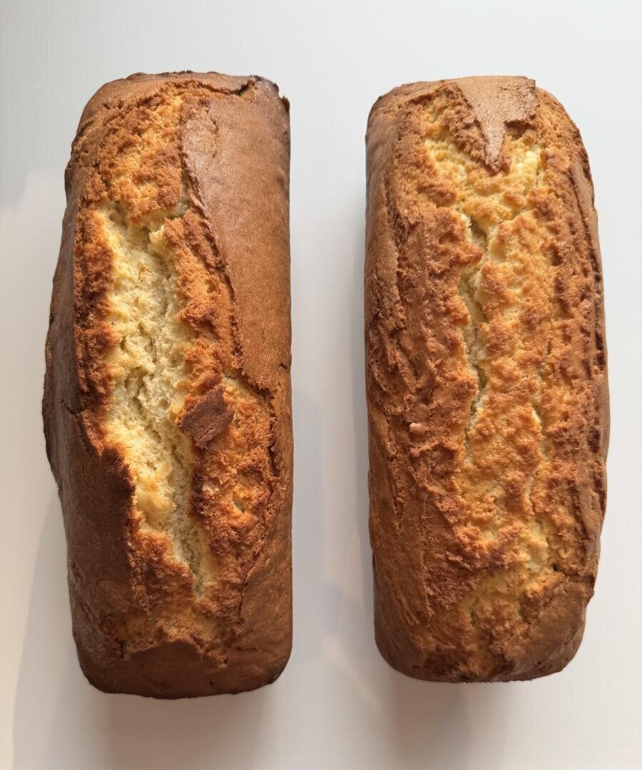 Two golden brown loaves of pound cake with cracked tops are placed side by side on a white surface. The loaves have a slightly rough texture and are evenly baked.