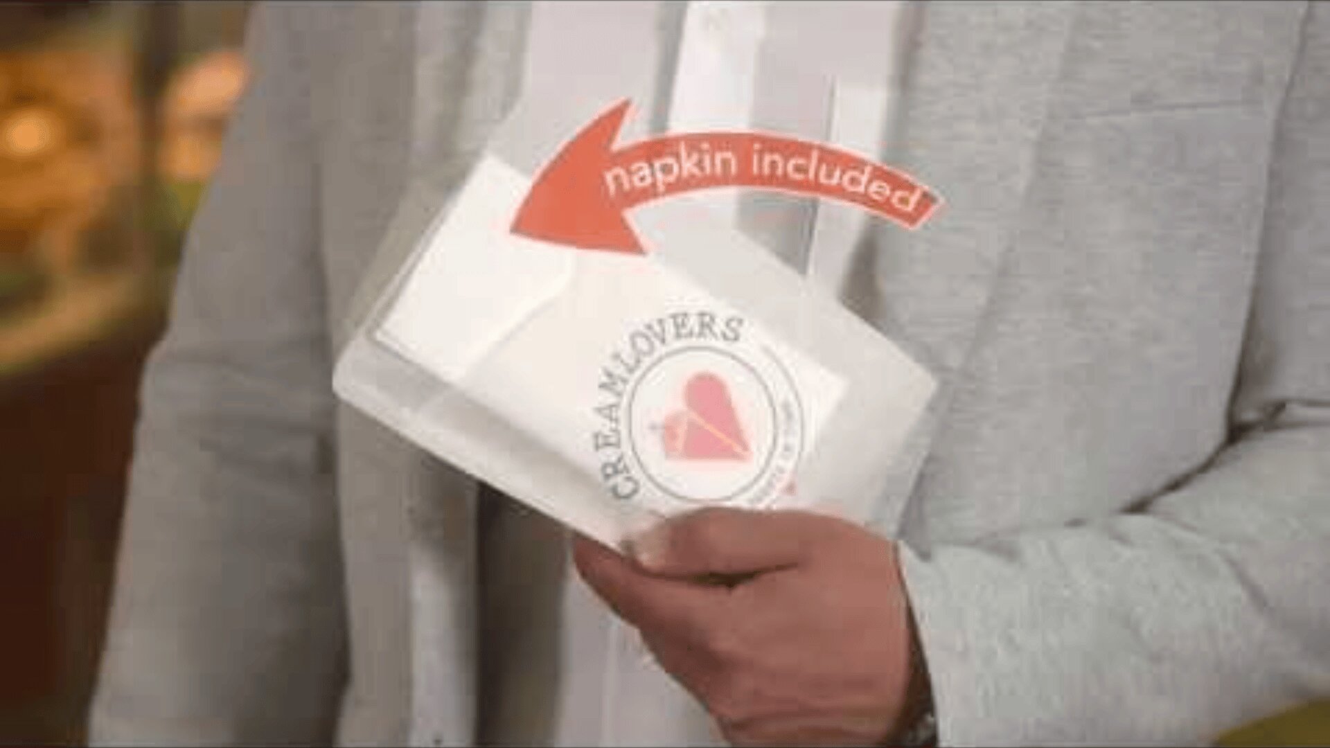 A person in a light gray blazer holds a paper-wrapped item with the CREAMLOVERS logo and a heart. An arrow points to a napkin with the text napkin included.