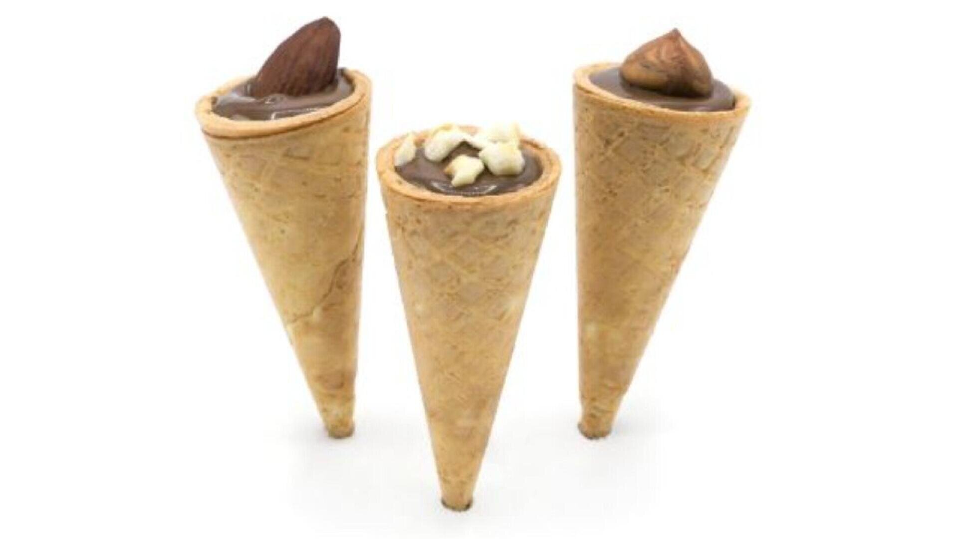 Three waffle cones filled with chocolate cream are arranged upright. Two cones are topped with whole nuts, and the middle cone is topped with chopped nuts. The background is plain white.