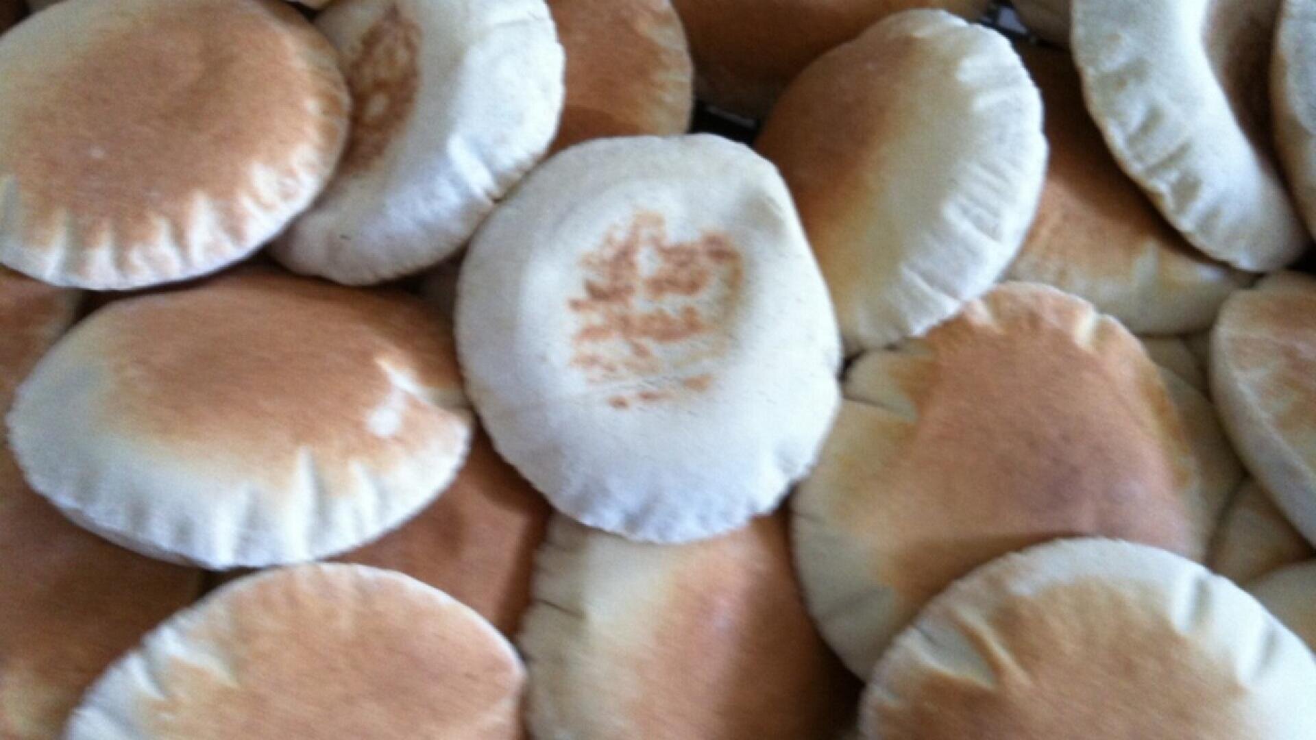 Ein Stapel frisch gebackener Fladenbrote, rund und bauschig, mit goldbrauner Oberseite und hellerem Rand, dicht an dicht gestapelt.