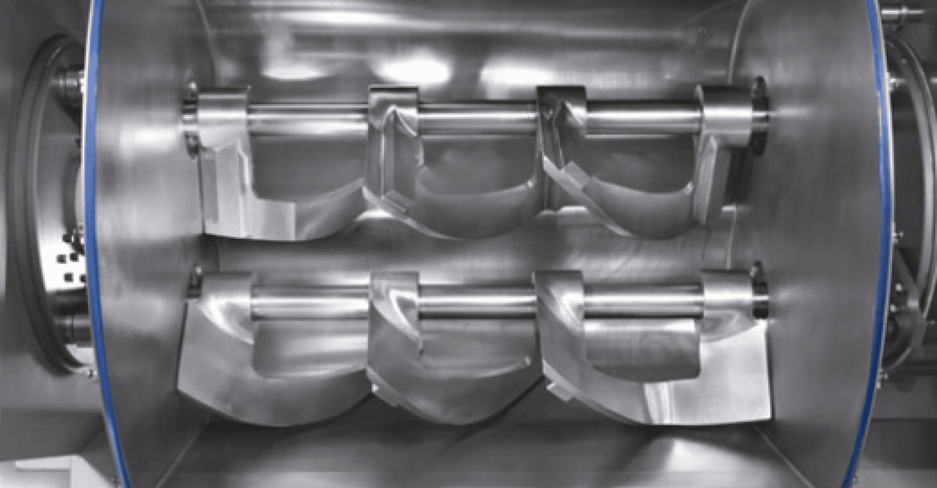 Close-up of a stainless steel industrial mixer with rotating paddles used for mixing or kneading materials in a cylindrical chamber.