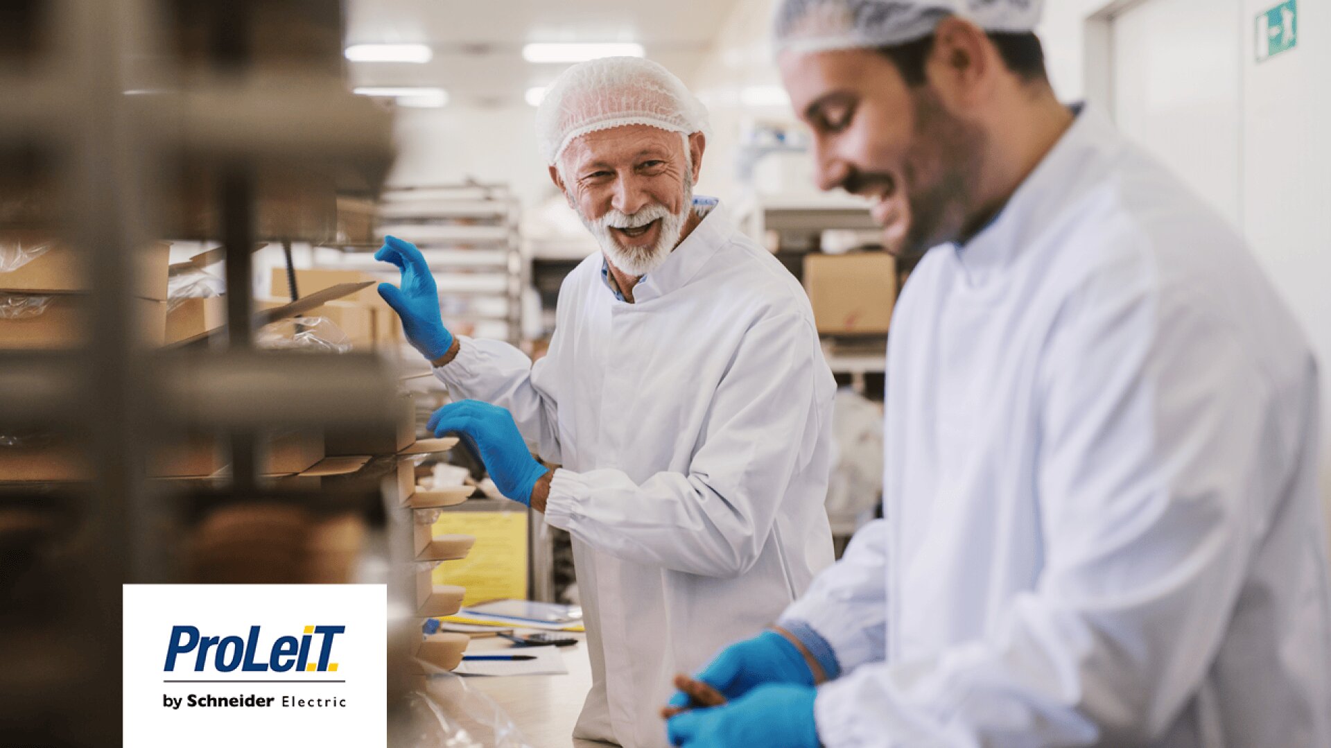 Two men wearing white lab coats, hairnets, and blue gloves smile while working in a food production facility. The ProLeiT by Schneider Electric logo appears in the bottom left corner.