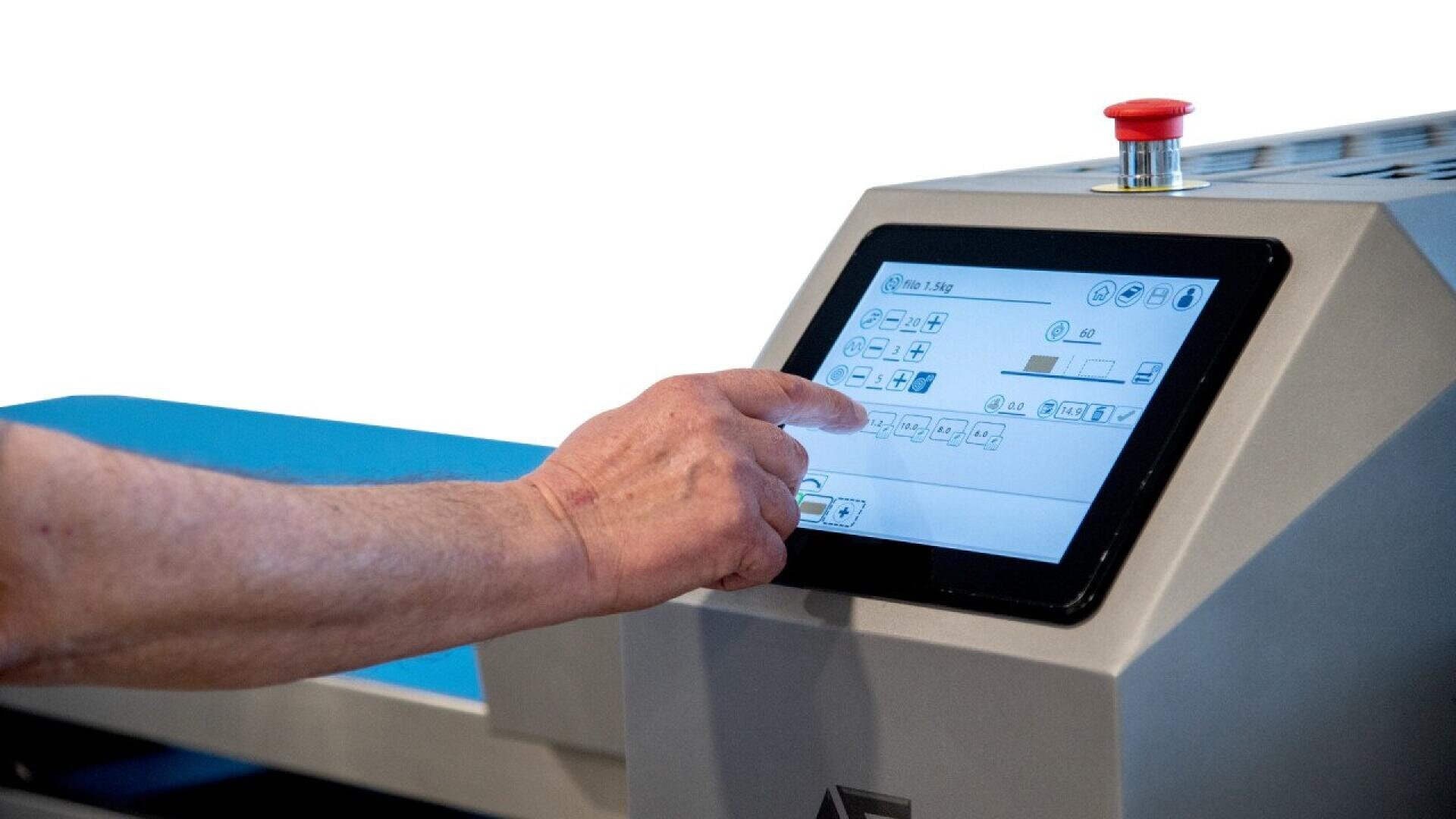 Eine Person bedient ein Touchscreen-Bedienfeld einer Industrieanlage, auf dem ein roter Not-Aus-Knopf zu sehen ist, der oben auf der Maschine angebracht ist.