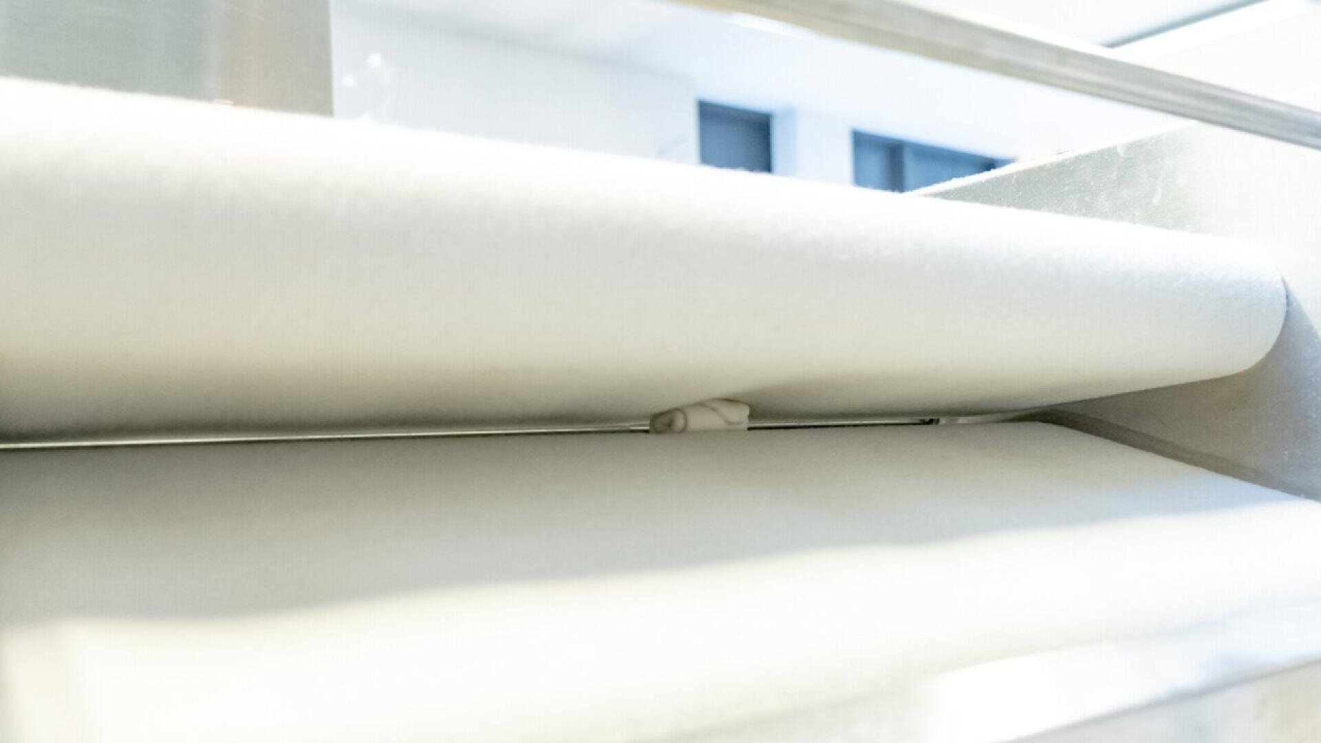 Eine Nahaufnahme eines kleinen Teigstücks, das in einer handelsüblichen Teigausrollmaschine zwischen zwei großen Walzen gepresst wird, mit einem hellen, sauberen Hintergrund.