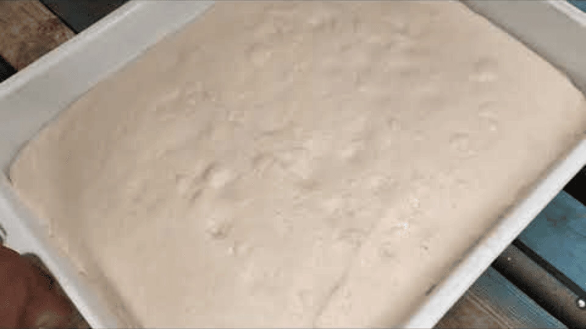Ein großer rechteckiger Behälter, gefüllt mit aufgegangenem Brotteig, mit glatter, leicht blasiger Oberfläche.