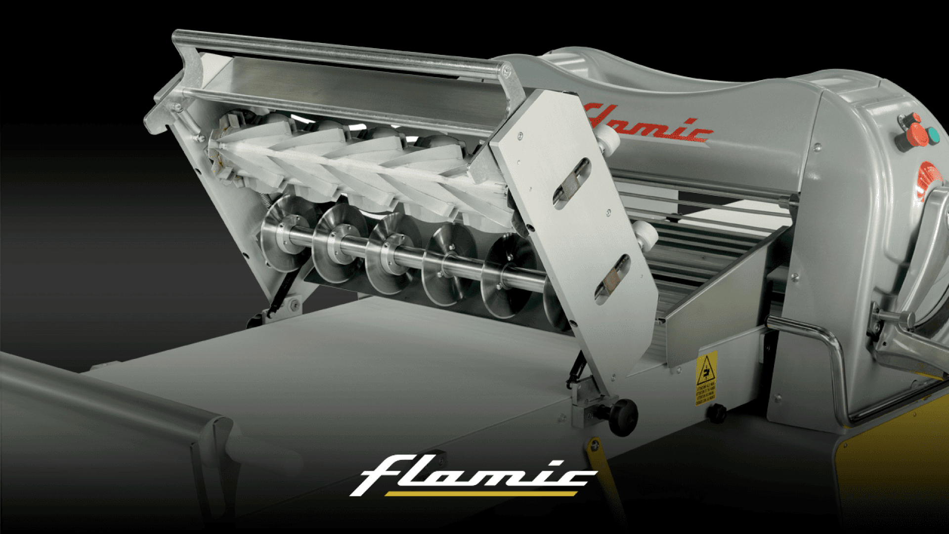 A close-up view of an industrial dough sheeter machine with metal rollers and blades, used for processing dough. The flamic logo is visible at the bottom of the image.