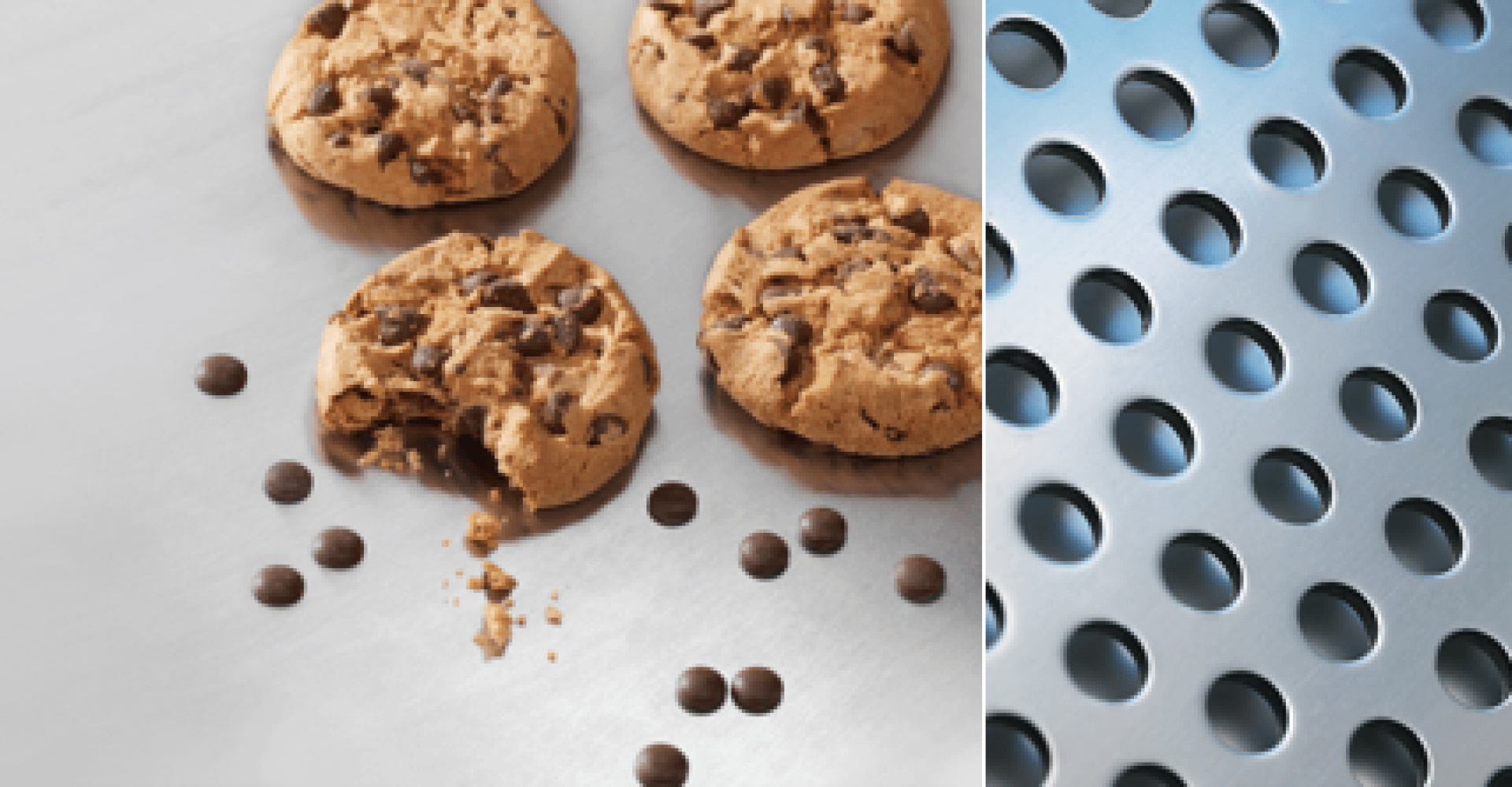Four chocolate chip cookies and scattered chocolate chips rest on a stainless steel surface, with one cookie partially eaten. Next to them is a shiny metal sheet with evenly spaced round holes.