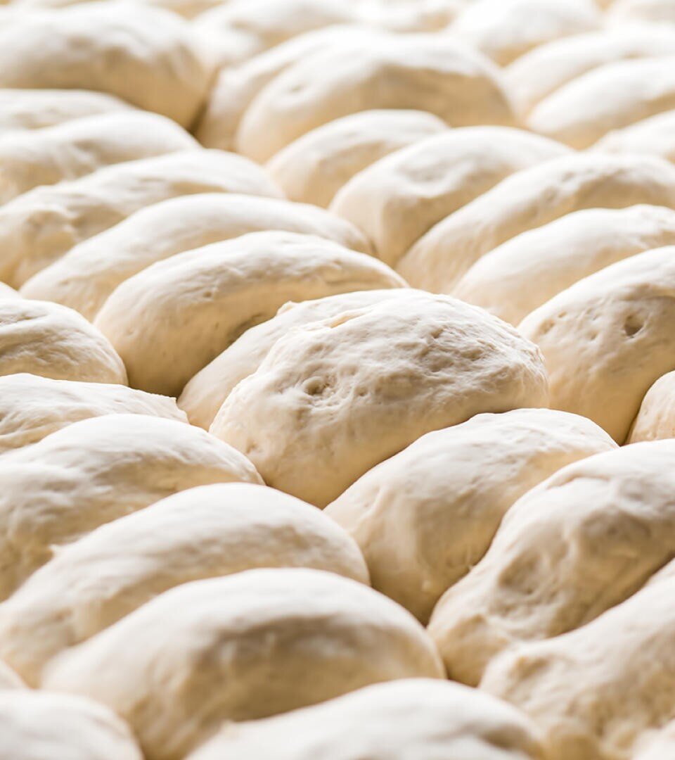 Reihen von ungebackenen Teigkugeln, die dicht aneinandergereiht eine weiche, glatte Textur aufweisen und bereit zum Backen sind.