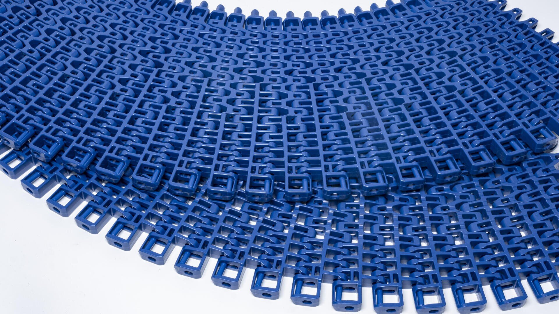 Close-up of interlocking blue plastic conveyor belt segments arranged in an overlapping, semicircular pattern on a white background.