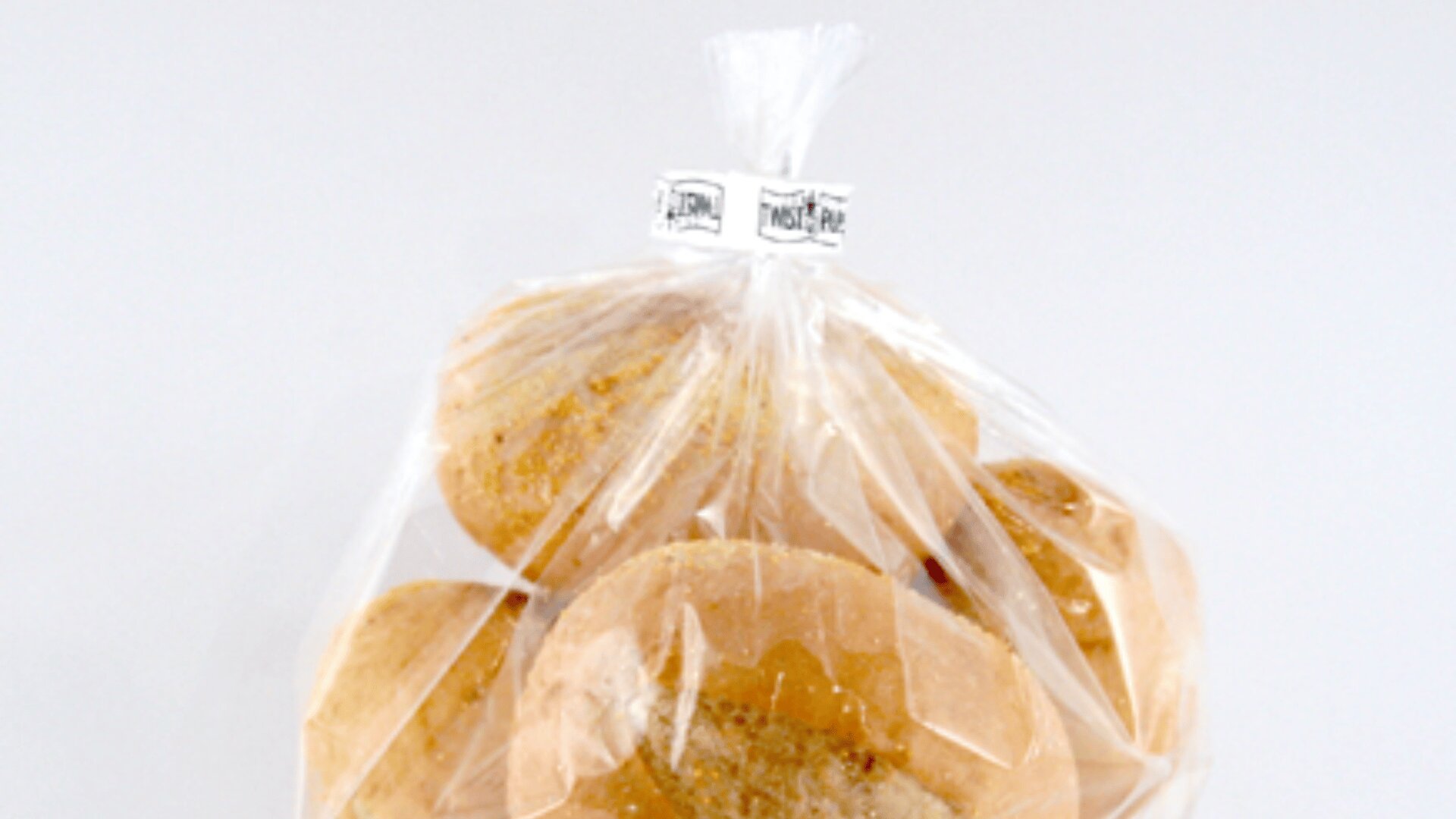 Eine durchsichtige Plastiktüte, gefüllt mit mehreren runden Brötchen, oben mit einem Drehverschluss verschlossen, vor einem schlichten weißen Hintergrund.