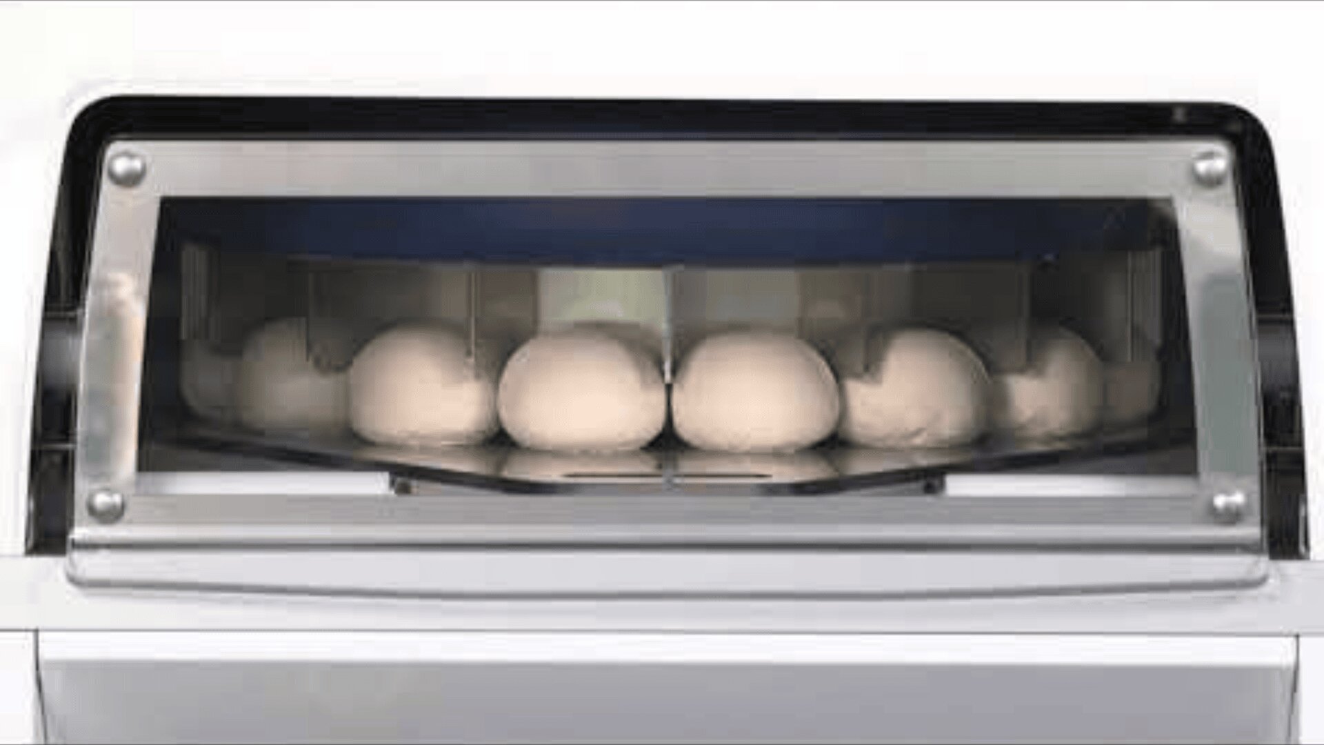 In einer Gärmaschine sind mehrere runde Teigkugeln aufgereiht, die durch ein transparentes Fenster zu sehen sind.