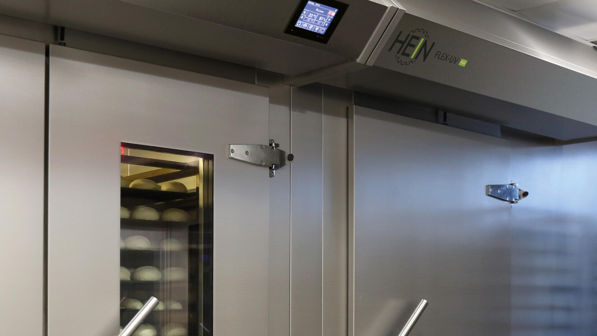 Ein gewerblicher Backofen mit einer Glastür, in der sich runde Brotteigschalen befinden, mit Metallgriffen, einem Bedienfeld und dem HEN FLEXI-Schriftzug auf der Oberseite.
