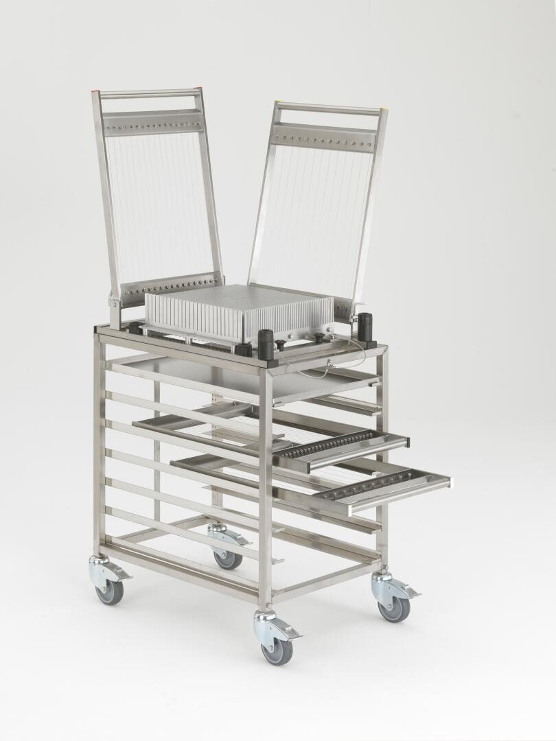 Eine Drahtschneidemaschine aus rostfreiem Stahl mit zwei erhabenen Schneidegittern, die auf einem Rollwagen mit offenen Regalen montiert ist, steht vor einem schlichten weißen Hintergrund.