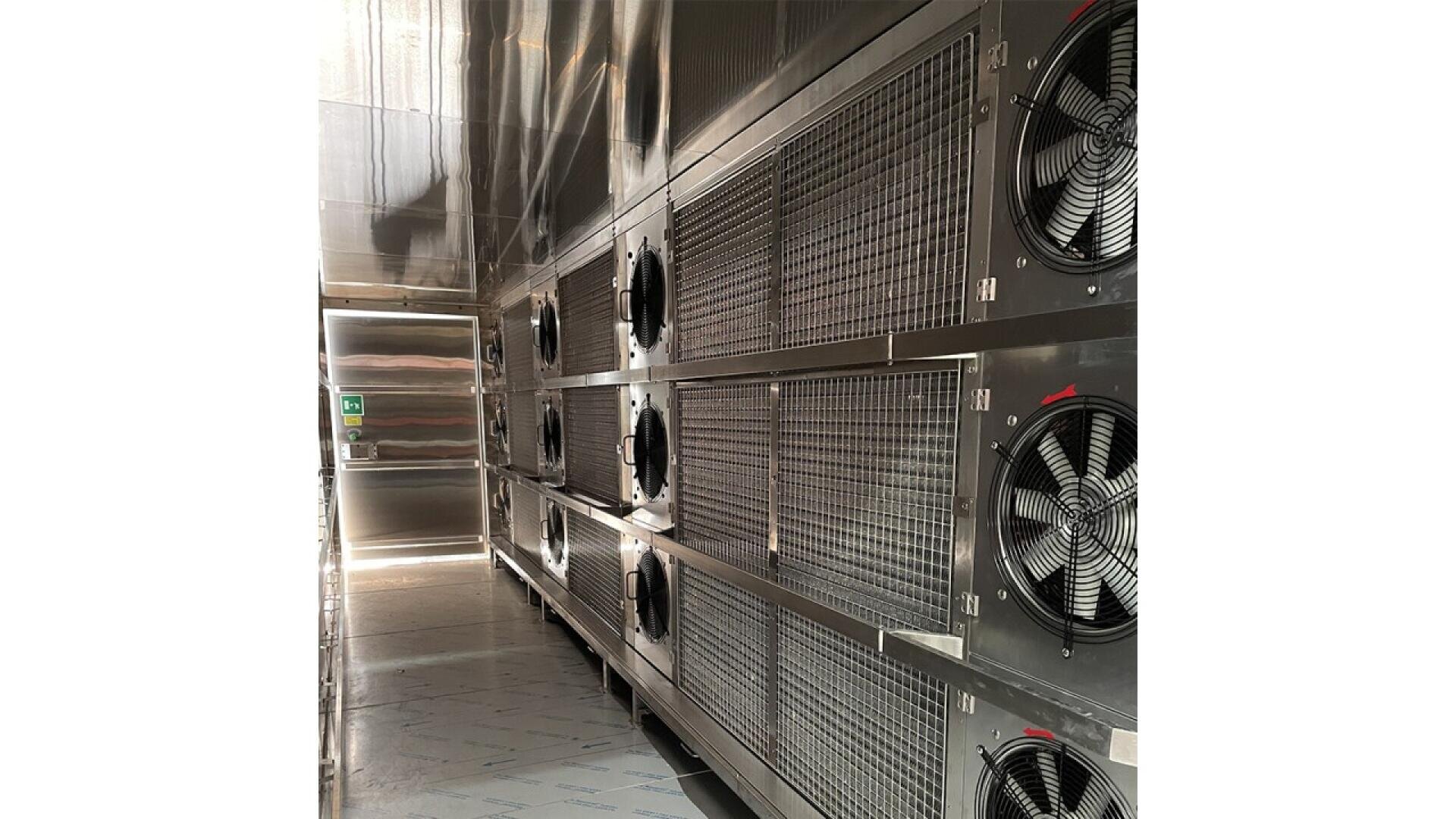 Eine Reihe großer industrieller Metalllüfter und -gitter ist an der Wand eines modernen, hell erleuchteten Gebäudes mit metallischen Oberflächen und einer Decke über dem Kopf angebracht.