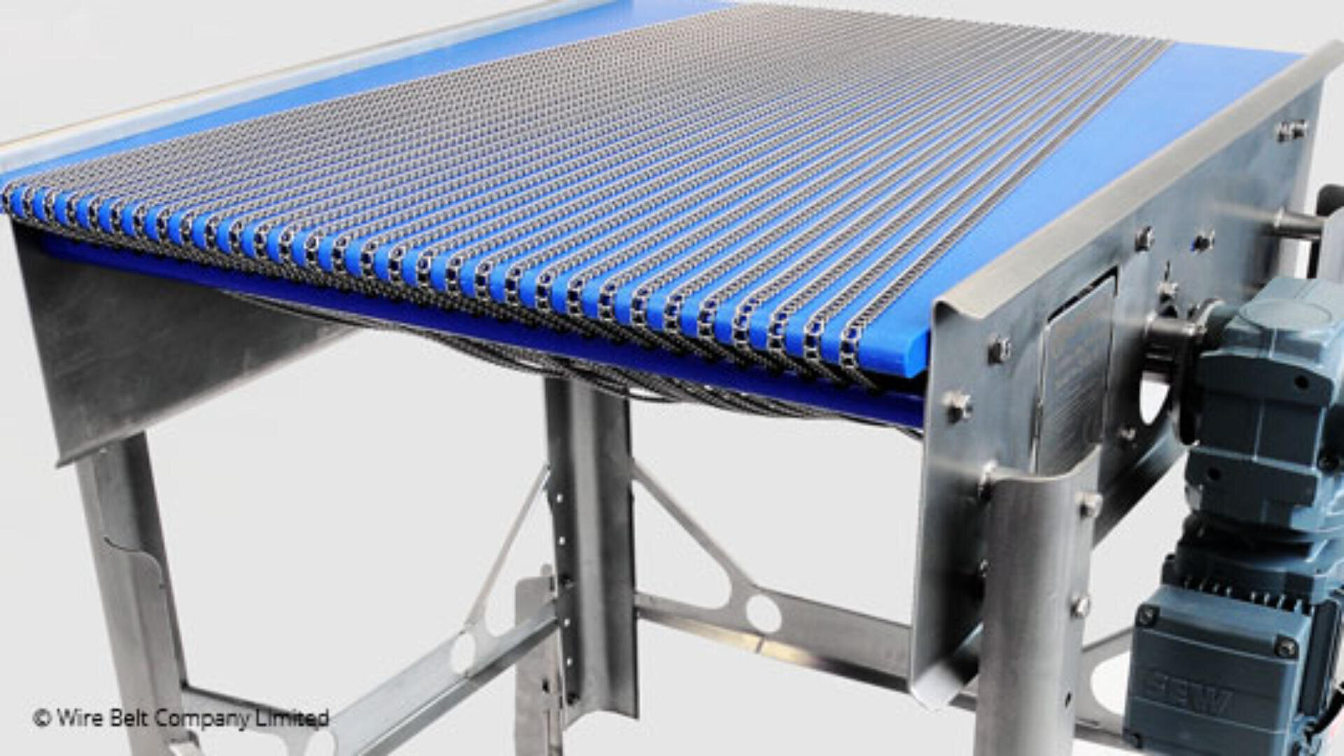 A stainless steel conveyor belt system with a blue surface and metal wire mesh, supported by a metal frame and powered by a motor on the right side.